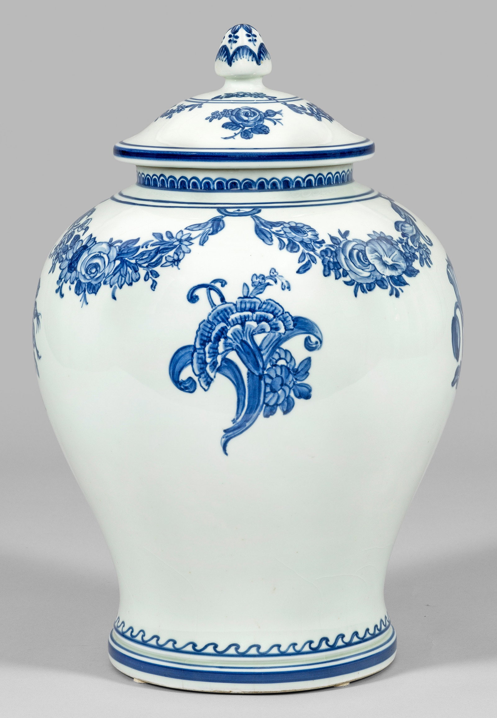 Große Unikat-Deckelvase mit Blaumalerei von Oluf Jensen: Graustichiger Scherben. Balusterform mit Haubendeckel. Oberhalb der Wandung Einzelblumen und Blütenfestons. Standring und Abschluss mit Wellen- bzw. Schuppenbordüre. Unterglasurblaue Malerei. Dekor-