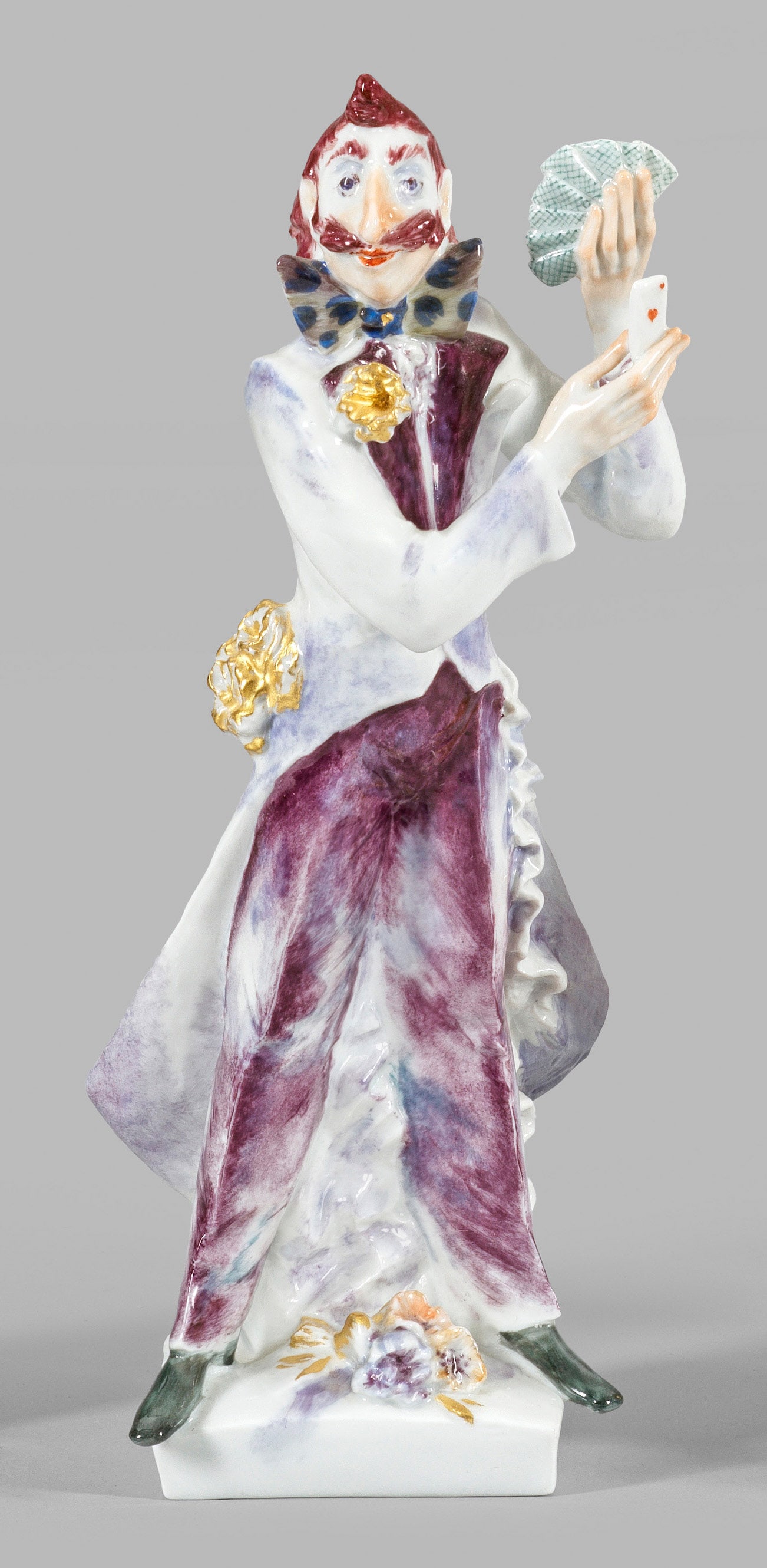 Zauberer mit Karten von Peter Strang: Auf gerundetem Rechteckssockel stehender Zauberer in langem Frack, Spielkarten in den erhobenen Händen haltend. Auf dem Boden Blumen liegend. Polychrome Malerei mit dezenter Goldstaffage. Entw. Peter