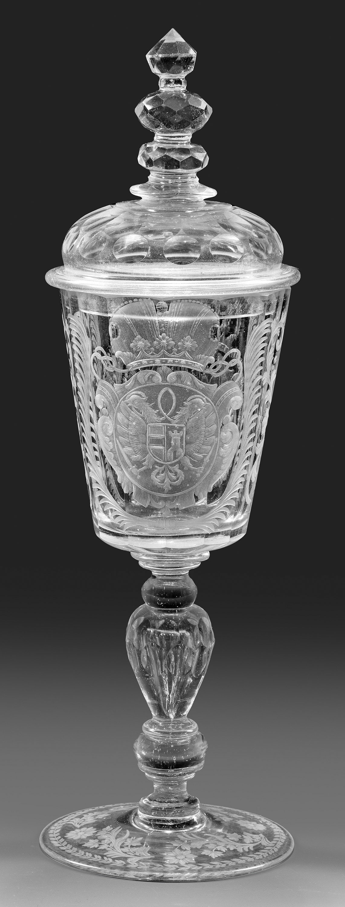 Historisch bedeutender Deckelpokal mit Habsburger Wappen: Farbloses Glas, partiell geschliffen. Scheibenfuß mit Abrissnarbe im Boden, Balusterschaft mit eingestochener Luftblase. Auf der facettierten Kuppa mit zwei Wappenkartuschen bzw. Hoheitszeichen in Ma