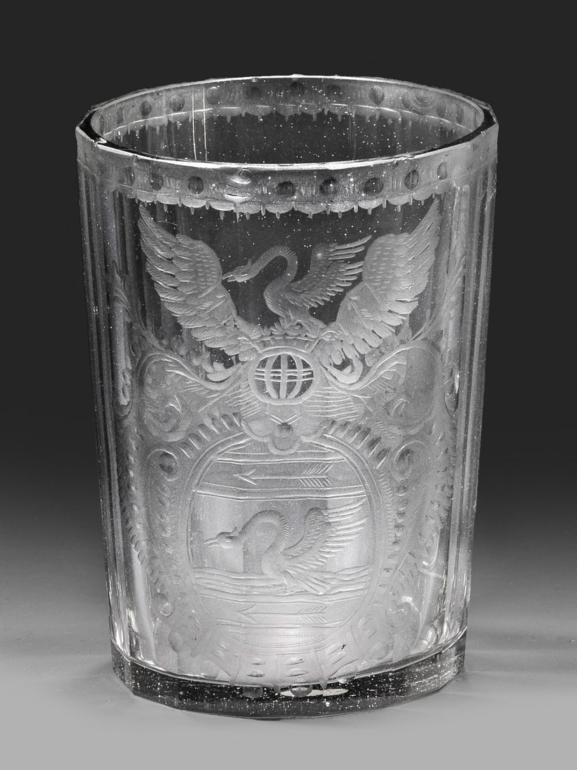 Böhmischer Barock-Becher mit Adelswappen: Farbloses Glas. Zylindrisch mit Facettenschälschliff. Dekor in Schliff und Mattschnitt, teilw. geblänkt, schauseitig ein Adelswappen mit Schwan. H. 10.8 cm. A Bohemian cut and engraved amorial glass