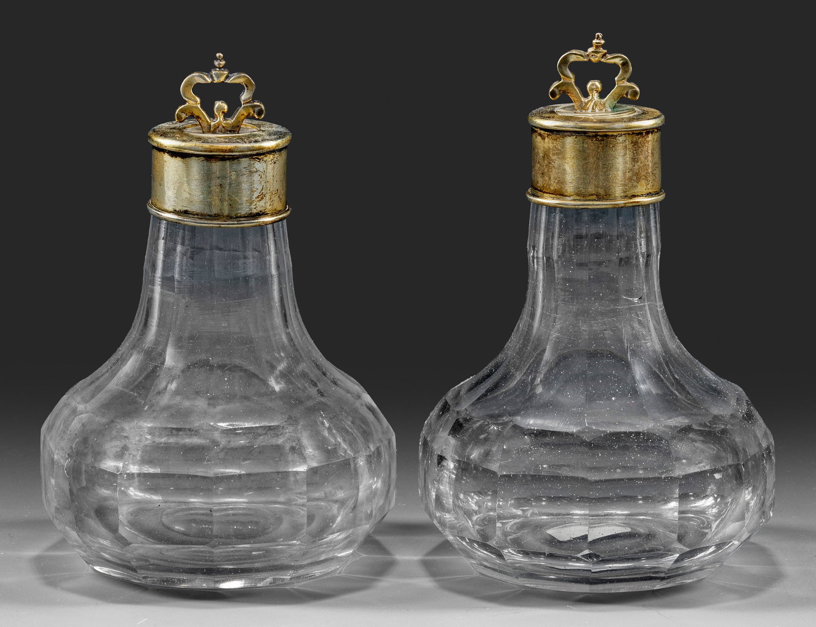 Paar Flakons oder kleine Karaffen mit Silbermontierung und: -stöpseln Birnform. Farbloses Glas mit ausgeschliffenem Abriss. Flächendeckender Facetten- bzw. Wabenfacettenschliff. Zylindrische, ober- und unterhalb profilierte Montierung aus vergoldetem Silber,