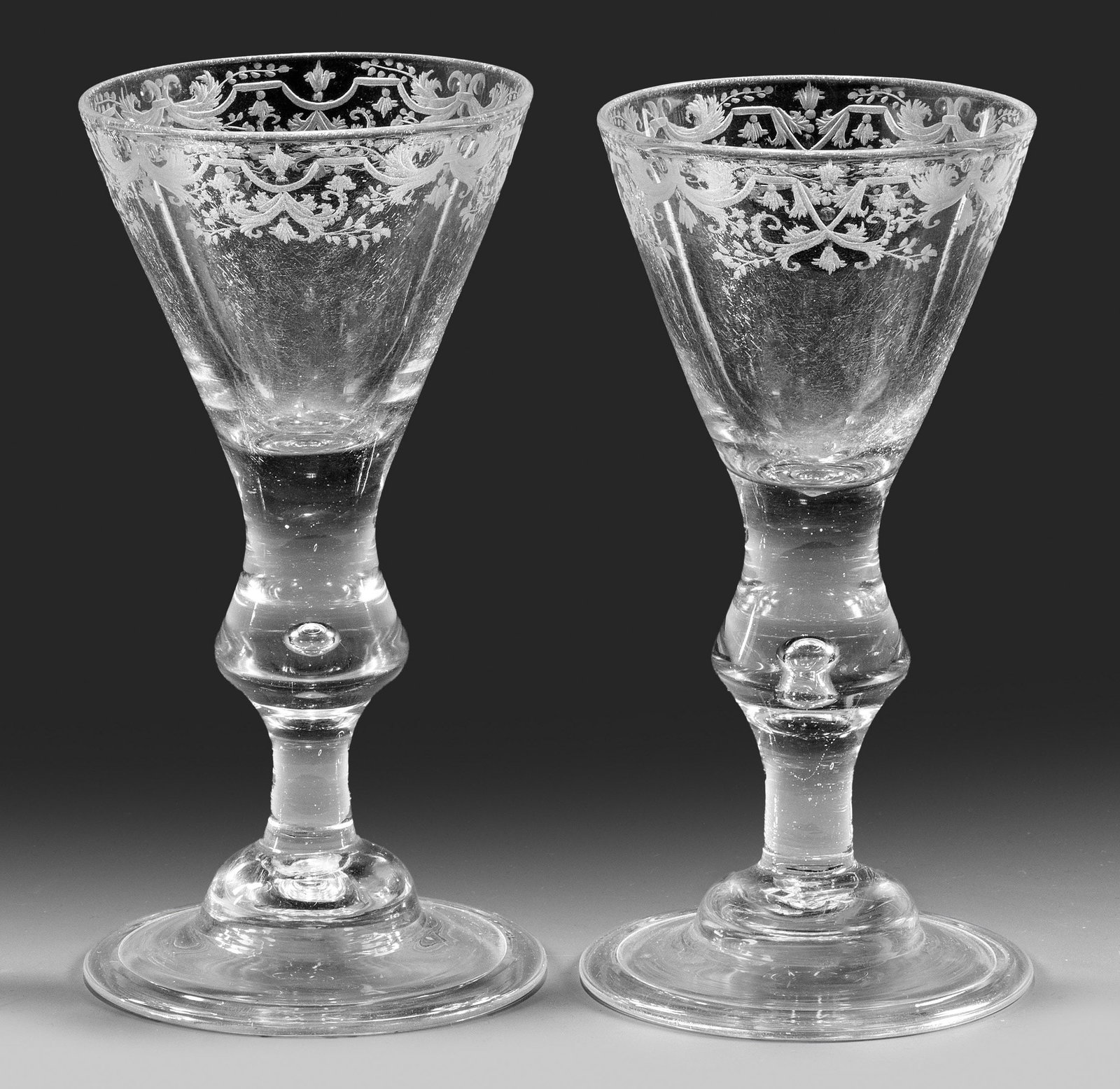 Paar Barock-Pokale mit Lambrequin-Dekor: Farbloses Glas. Leicht gewölbter Glockenfuß mit umgeschlagenem Rand, im Balusterschaft eingestochene Luftblase, der Lippenrand der konischen Kuppa akzentuiert durch eine umlaufende, fein geschnitten