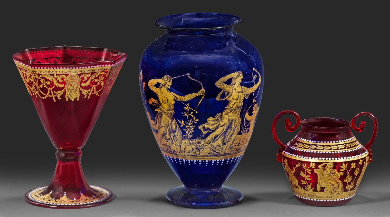 Kleine Kollektion von venezianischem Murano-Glas: 3-tlg.; Dunkelkobaltblaues bzw. rubinrotes Glas. Mythologischer bzw. ornamentaler Dekor im Renaissance-Stil, goldradiert und in weißer Emailmalerei. H. 7 cm-16,8 cm. A three-piece collection of Itali