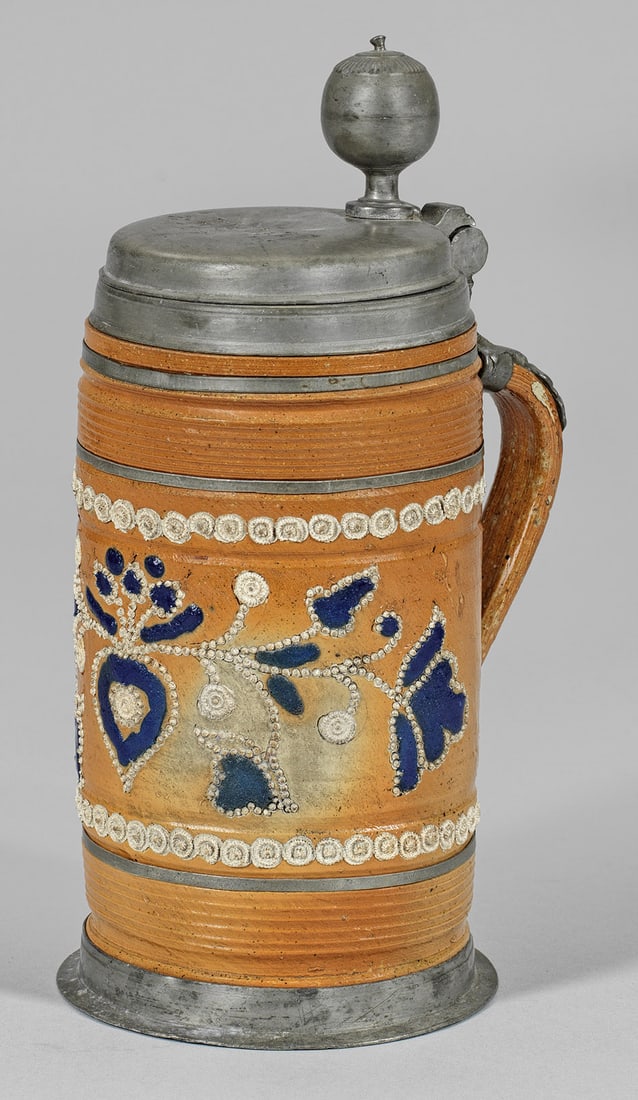 Altenburger Perlhumpen: Steinzeug, ockerfarbene Salzglasur. Durch Profilrillenbänder und Zinnreifen gegliederte Walzenkrugform. Aufgelegter, weißgrauer Perldekor mit einem Herz und floralen Motiven, kombiniert mit dunkelbl