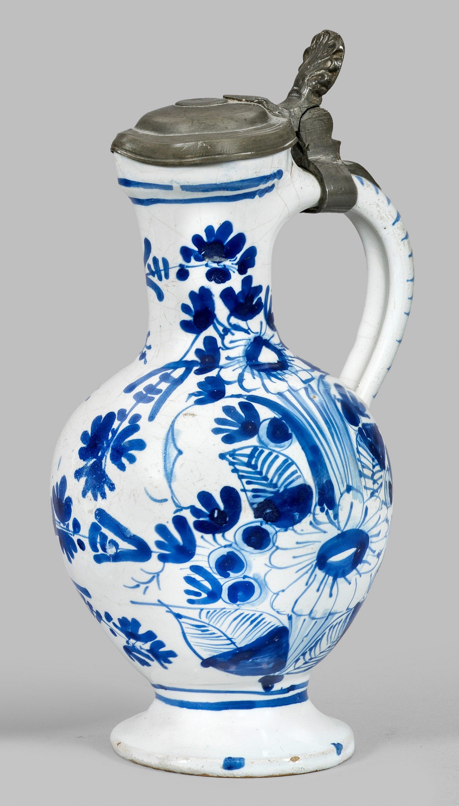 Hanauer Enghalskanne mit Blumendekor: Fayence. Balusterförmiger Korpus mit seitlichem Ohrhenkel und spitz zulaufender Tülle. Kobaltblauer Scharffeuerdekor. Schauseitig der Wandung üppig empor wachsende Blumenstauden, begrenzt durch Rin