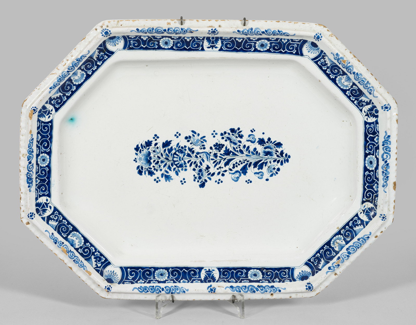 Große Anbietplatte mit Lambrequin-Dekor: Fayence. Oktogonale Form mit vertieftem Spiegel. Zentral eine Blütenstaude, auf der Fahne Lambrequin-Dekor in monochromer blauer Malerei. Minim. best.; Manufakturmarke. 49 cm x 36 cm. Provenienz: Auf