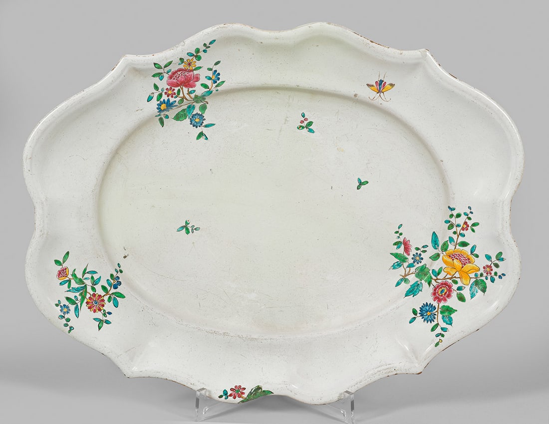 Große Fayenceplatte mit Indianischem Blumendekor: Ovale, passig geschweifte, leicht vertiefte Form. Im Übergang von Spiegel und Fahne ostasiatisch inspirierte Blüten und Schmetterlinge in polychromer Muffelmalerei. Rest./ber.; Manufakturmarke "F". 