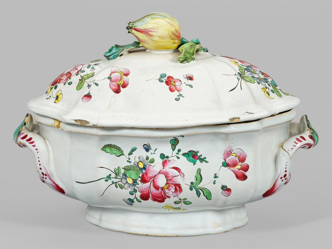 Deckelterrine mit Blumendekor: Fayence. Ovale, leicht fassonierte Form mit zwei seitlichen Henkeln, auf dem Deckel ein plastischer Granatapfelknauf. Polychromer Dekor in Muffelmalerei aus lockeren Blumengebinden und gestreuten Blü