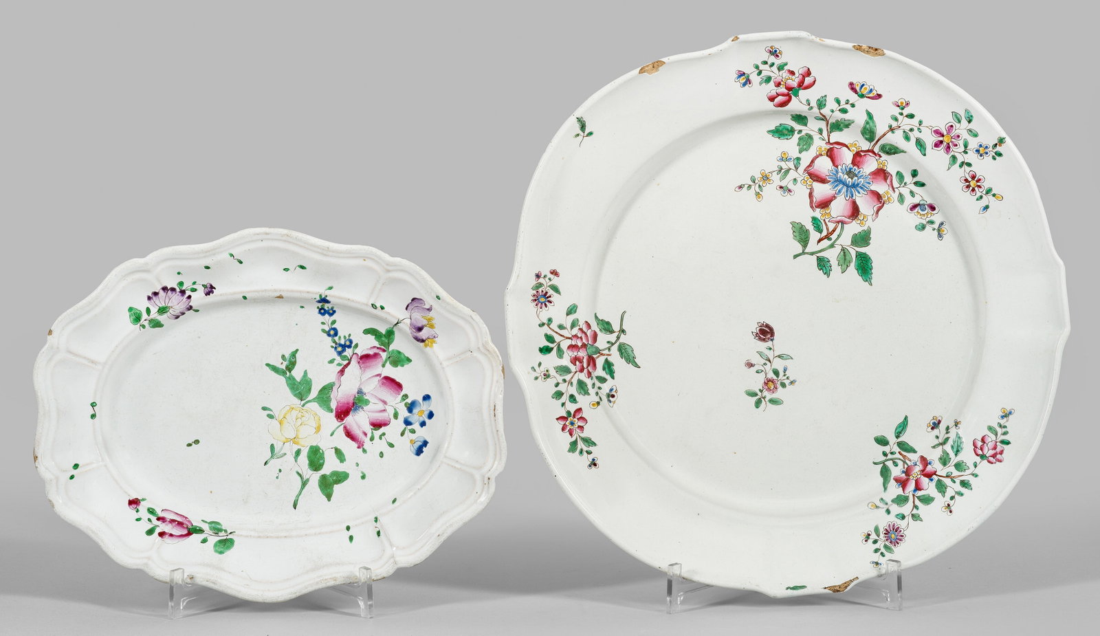 Zwei Straßburger Anbietplatten mit Blumendekor: Fayence. Ovale bzw. runde, leicht vertiefte Form mit teilw. fassonierter, geschweifter und gerippter Fahne. Im Spiegel und auf der Fahne Blumengebinde in polychromer Muffelmalerei. Glasurkrakelee. Par
