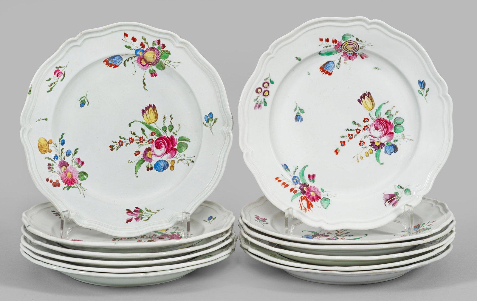 Zwölf Teller mit Blumendekor: Fayence, graustichiger Scherben. Runde, leicht vertiefte Form mit passig geschweiftem, profiliertem Rand. Im Spiegel und auf der Fahne farbenprächtige Blumengebinde in polychromer Muffelmalerei. Mini