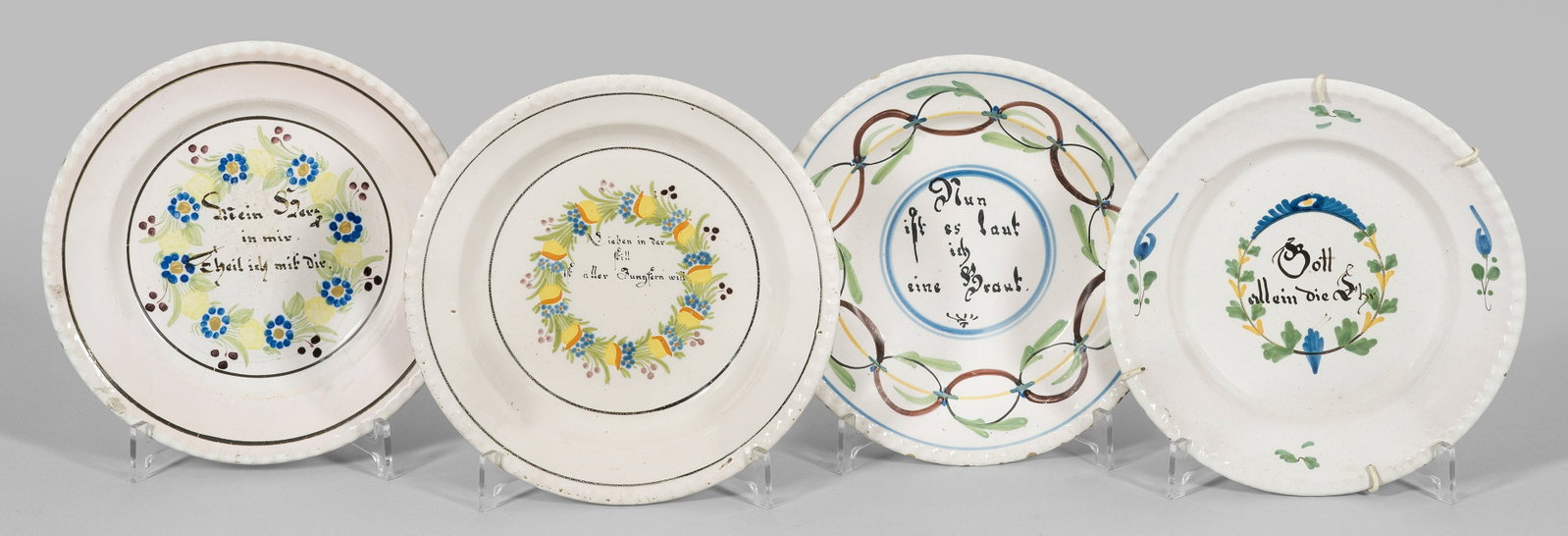 Vier Teller mit Sinnsprüchen: Fayence. Runde Form mit leicht reliefiertem Rand. Im vertieften Spiegel von einem floralen Blütenband gerahmtes Rund mit Sinnsprüchen. Polychrome Scharffeuermalerei. Manufakturmarke "W", "B" und umg