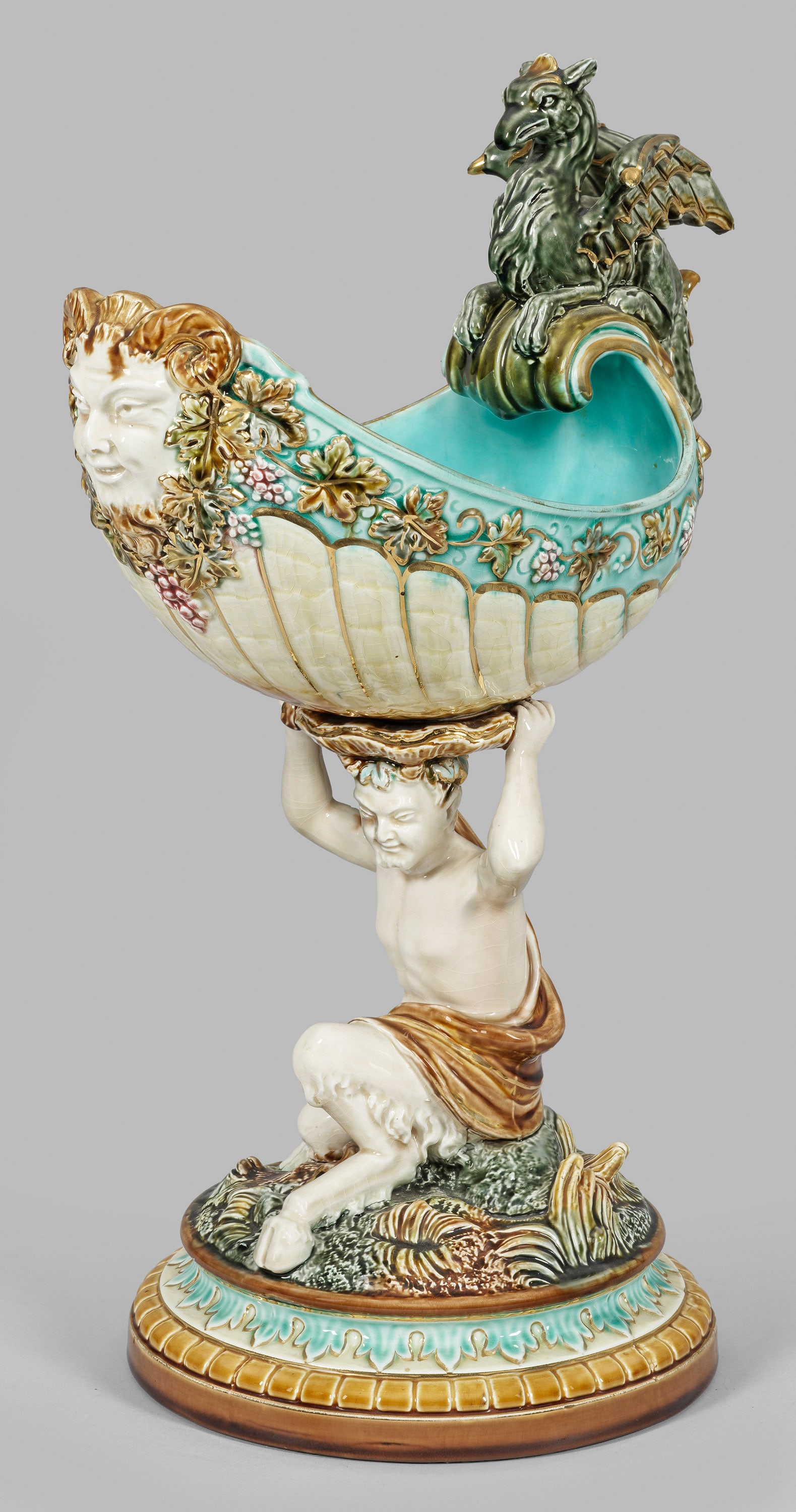 Prächtiger Nautiluspokal im Renaissance-Stil: Steingut. Plastisch gestalteter Schaft in Gestalt eines sitzenden Fauns, die mit Weinreben reliefierte Nautilusschale mit Greifenhenkel und Faunmaskaron. Polychrome Unterglasurmalerei mit Goldstaffage