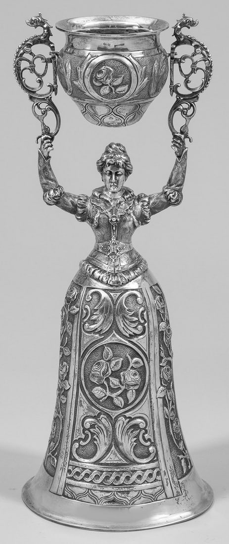 Monumentaler Historismus-Brautbecher: Silber. Vollplastische Darstellung einer Frauenfigur im Renaissancekleid, der glockenförmige Rock als Kuppa dienend. In den erhobenen Händen, zwischen zwei durchbrochen gearbeiteten, volutierten Bü
