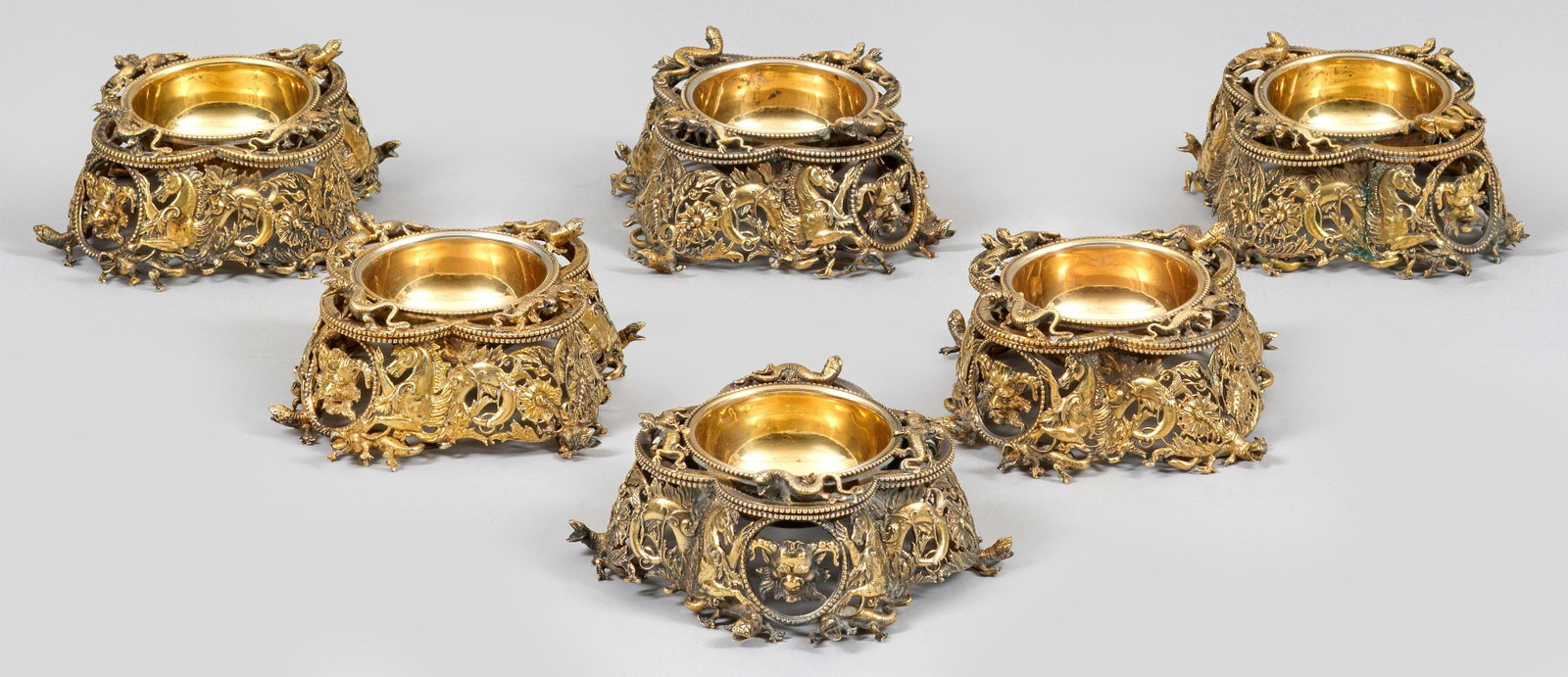 Sechs Historismus-Salieren: Silber, vergoldet. Vierpassige Grundform mit vertieft eingelassener runder Kuppa. Die äußere Wandung durchbrochen gearbeitet mit Hippokampen, Faunmaskarons und Blattwerk. Rand und Stand besetzt mit 