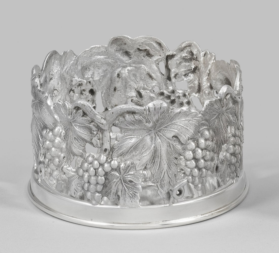 Flaschenuntersetzer: Silber. Zylindrische, durchbrochen gearbeitete Wandung, umzogen von reliefplastischen Weinreben und -ranken. Gest. 925. Gew. ca. 240 g. D. 10,5 cm. A German Sterling silver bottle stand. Standard mark