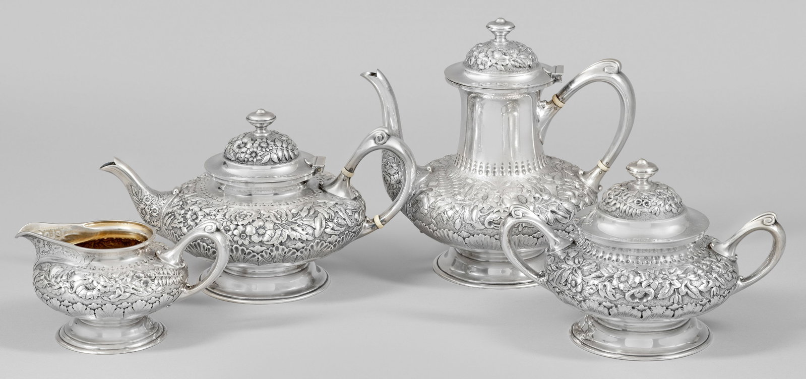 Tiffany Kaffee- und Teeservice: Plated. 4-tlg.; Kaffeekanne, Teekanne, Zuckerschale, Sahnegießer. Mehrfach profilierter Rundfuß, gedrückt bauchiger Korpus mit Blüten- und Palmettenrelief vor punziertem Grund, von mehreren Punktr