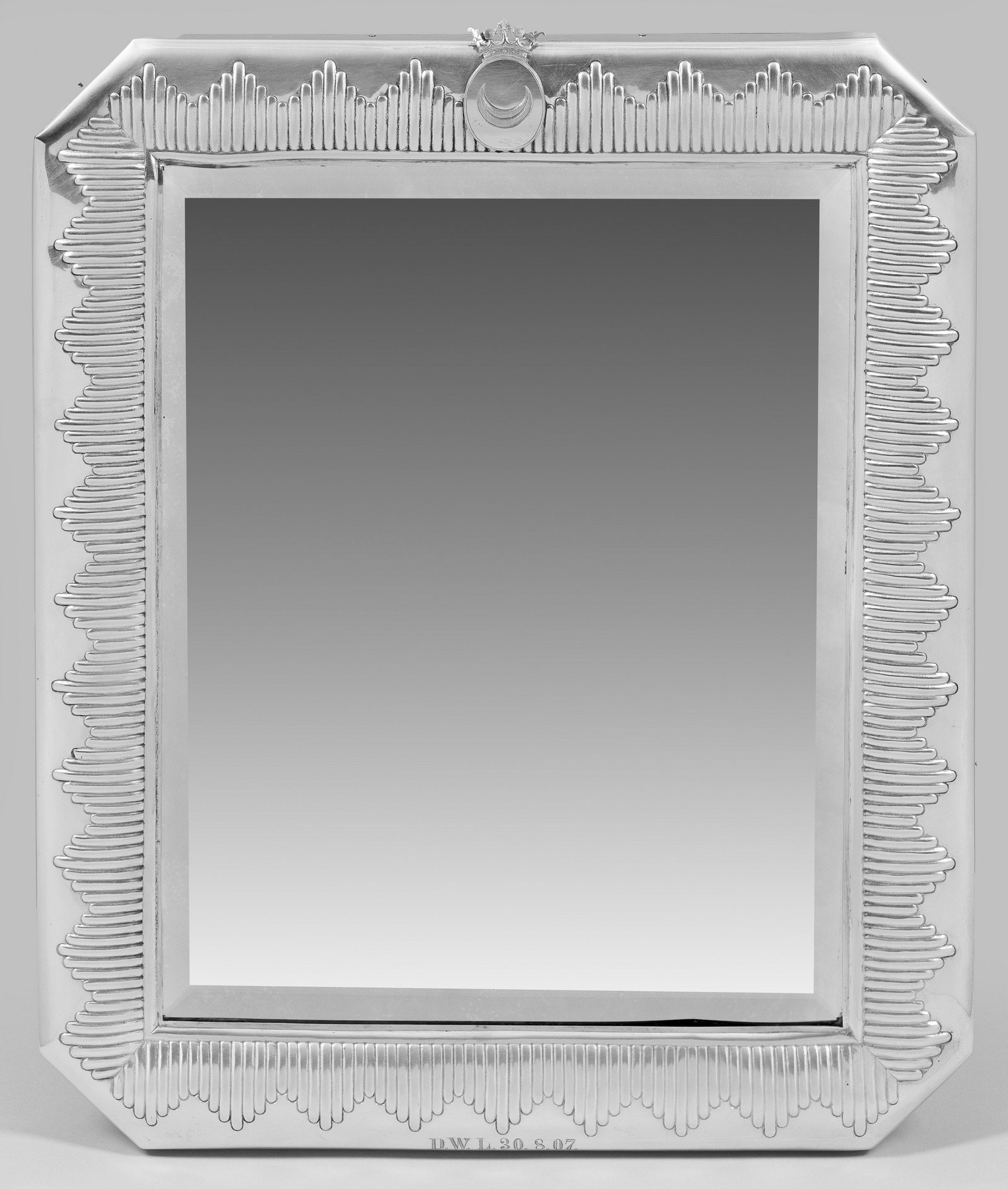 Großer Tischspiegel: Silber über Holzkern, Glas. Rechteckige Spiegelfläche, an den äußeren Ecken gekanteter Rahmen mit umlaufendem, reliefierten Zungendekor. Zentral oben am Rahmen ovale Wappenkartusche mit liegender 