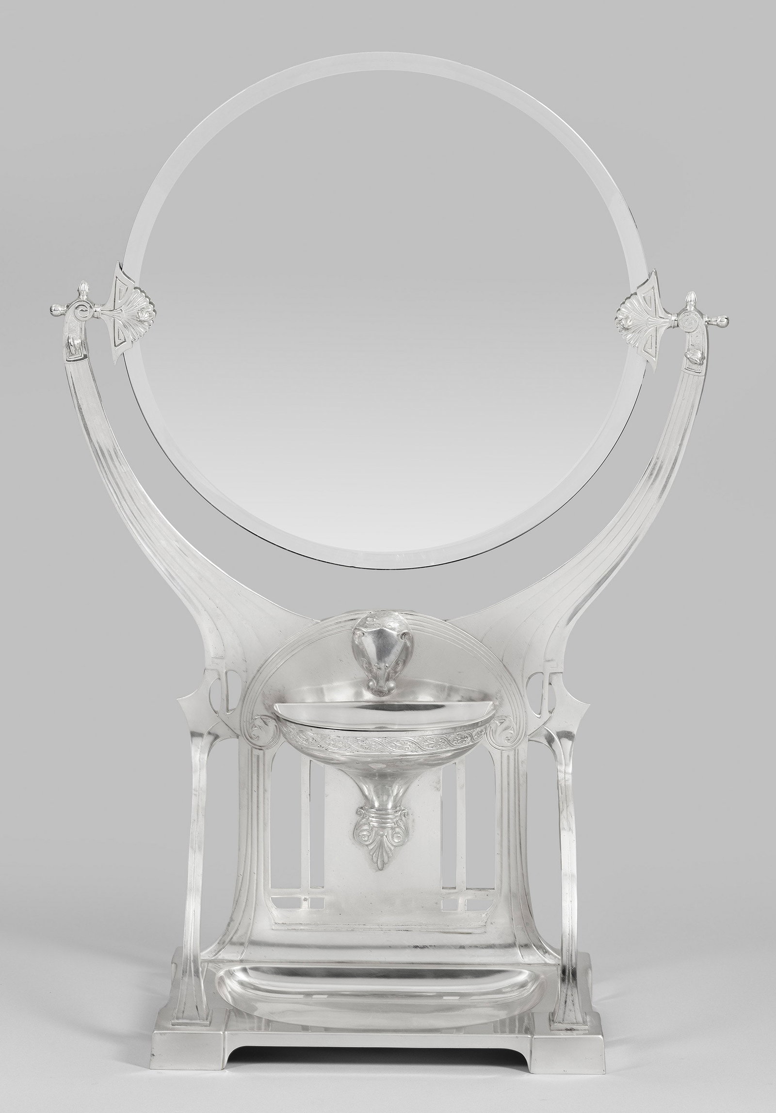 Jugendstil-Toilettespiegel: Plated und Spiegelglas. Beidseitig mit Stand verschraubte, runde Spiegelfläche, gehalten von zwei Palmetten. Stand durchbrochen gearbeitet mit vegetabil geschwungenen Linien, plastisch ausgearbeitete