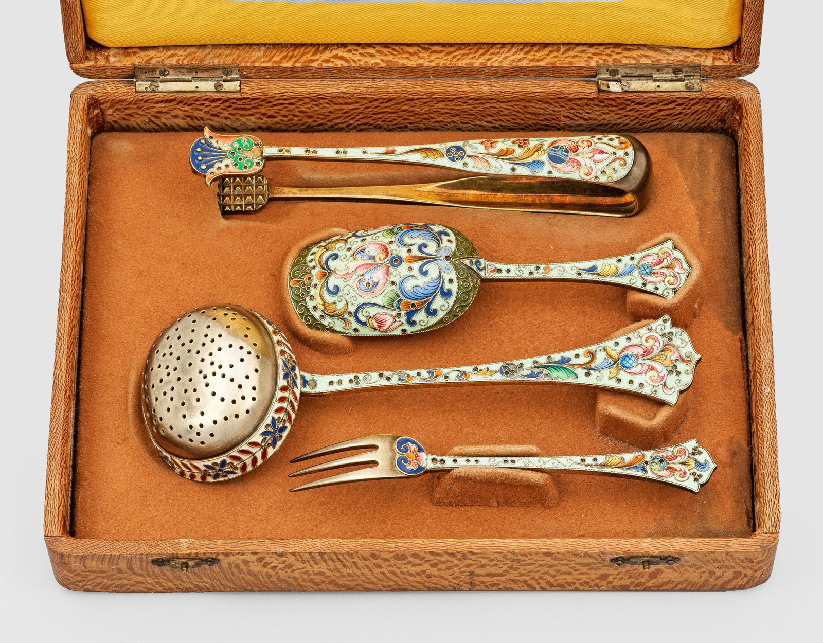 Cloisonné-Teebesteck: mit Etui. 4-tlg.; Silber, vergoldet und teilw. polychrom emailliert. Die geschweift endenden, konischen Griffe und teilw. die Rückseiten der Laffen nahezu flächendeckend floral und ornamental dekori
