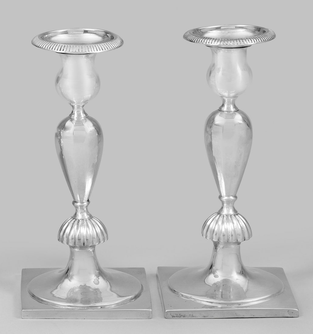 Paar Biedermeier-Tafelleuchter: Silber. Quadratische Plinthe, in rundem Fuß ansetzender, facettierter Balusterschaft mit senkrecht profiliertem Nodus und vasenförmige Tülle mit herausnehmbarer, weit ausschwingender Traufschale. P