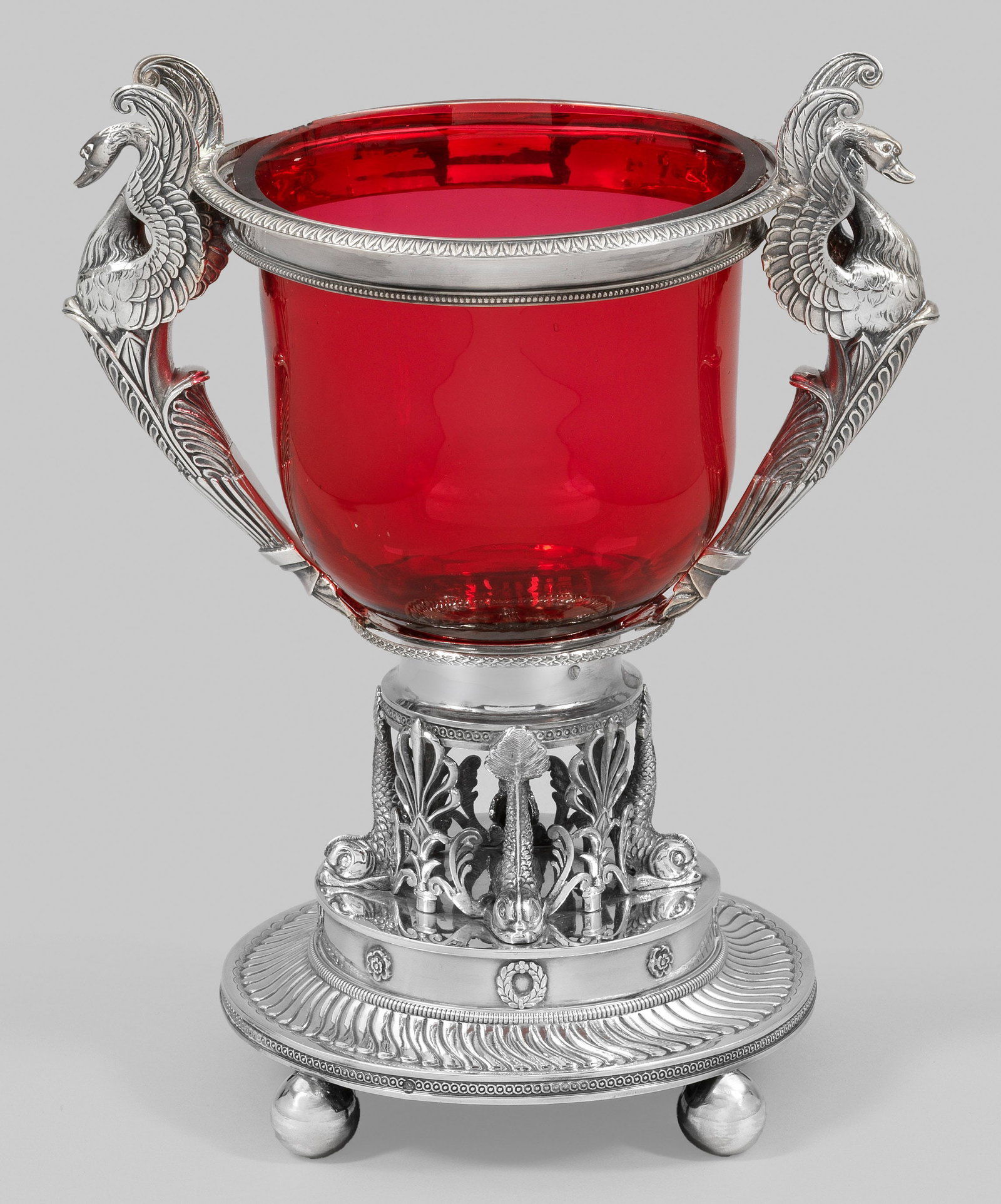 Charles X-Tafelaufsatz: Silber. Auf vier Kugelfüßen runder, mittig zylindrisch aufgewölbter Stand mit umlaufendem, gedrehten Zungenfries, Eierstab und kleinen applizierten Blumen und Lorbeerkränzen. Darauf von vier durch