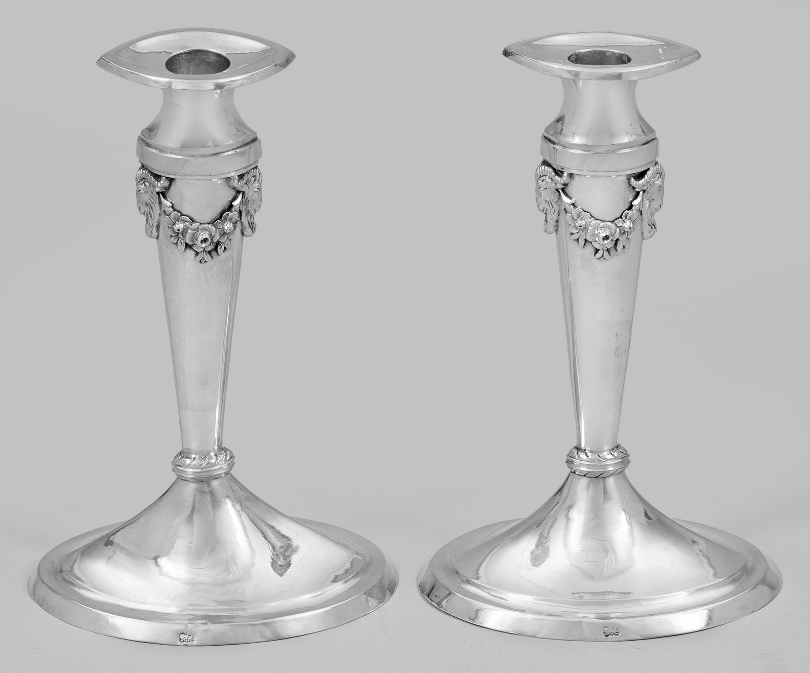 Paar elegante Empire-Tafelleuchter: Silber. Trompetenförmiger, ovaler Stand, durch zwei gedrehte Wülste verbunden mit konischem, spitzovalen Schaft. An der Schulter seitlich zwei halbplastische Widderköpfe, verbunden durch korrespond