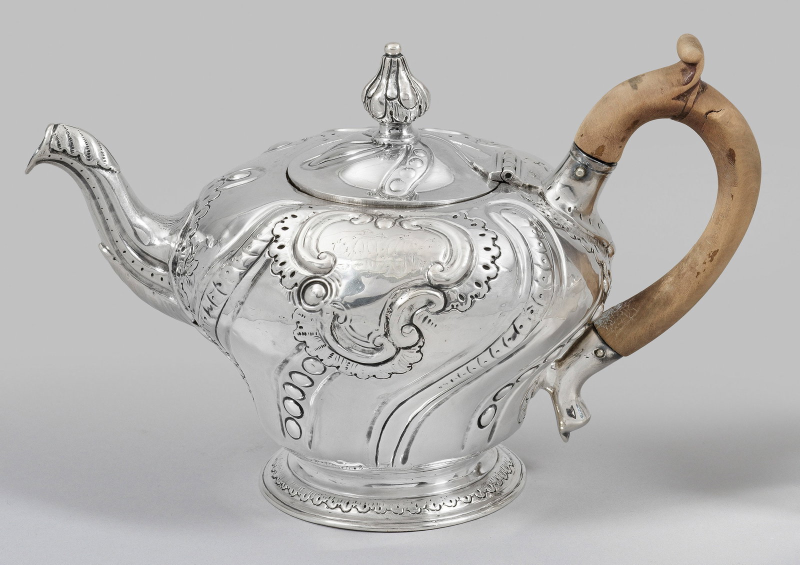 George III-Teekanne: Sterlingsilber. Auf rundem, ansteigendem Fuß, sich erweiternder, stark gedrückter Korpus mit hoch angesetztem, kurzem Ausguss. Ohrenhenkel aus Holz. Gering bombierter Scharnierdeckel mit Balusterkna