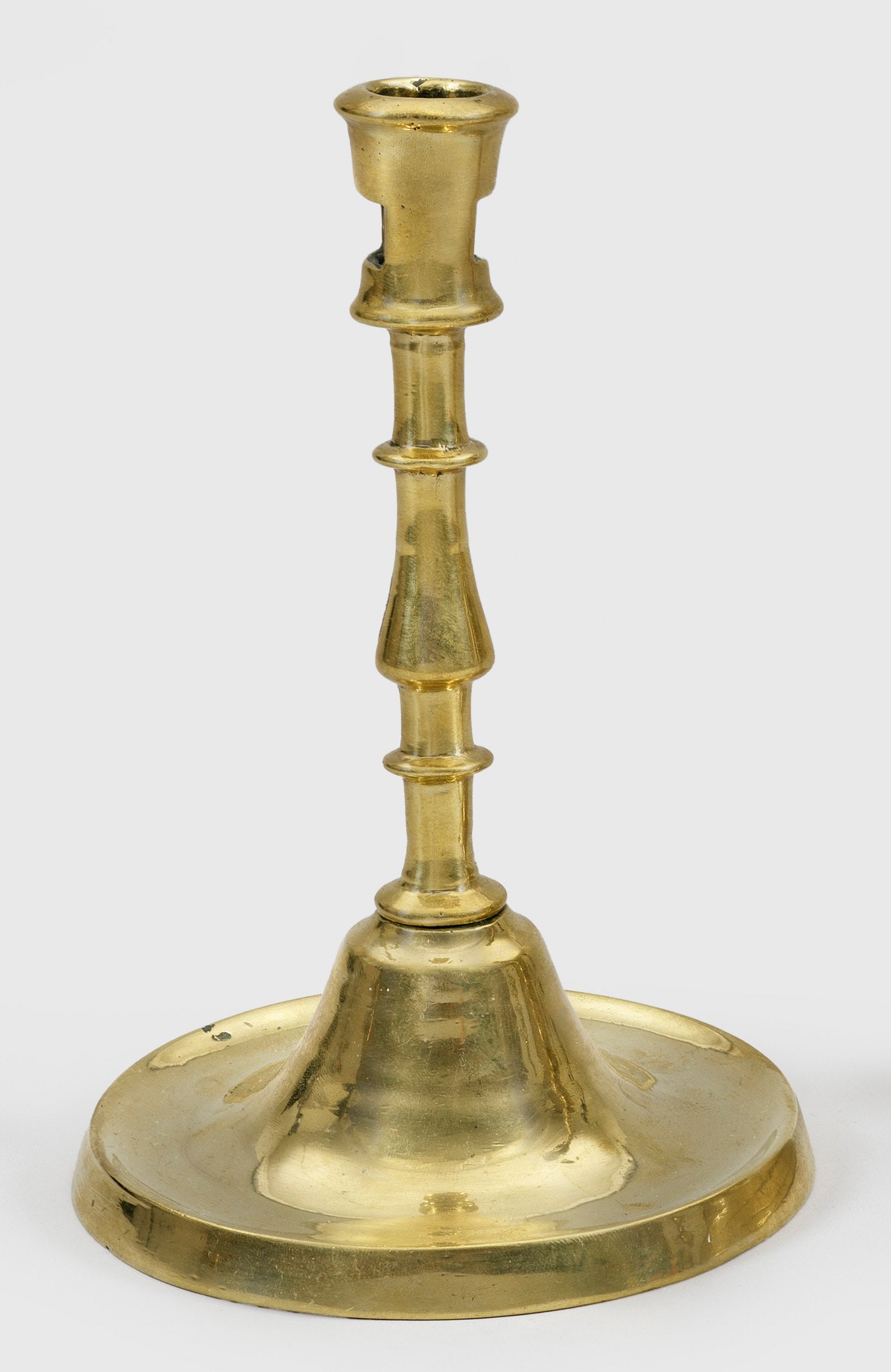 Spätgotischer Tischleuchter: Messing. Runder, flacher, mittig ansteigender Fuß, schlanker Schaft, gegliedert durch Nodus und Scheiben und leicht konische Tülle mit beidseitiger Reinigungsöffnung . H. 19 cm. Vgl. R. F.