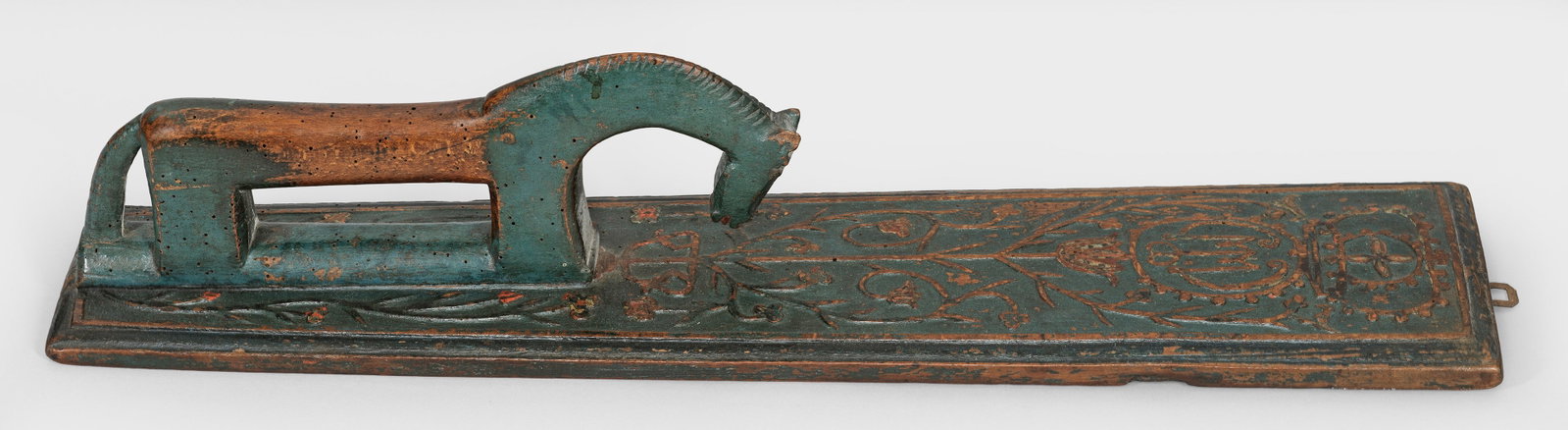 Mangelbrett mit Pferdegriff: Holz, geschnitzt, teilw. dunkelgrün gefasst. Rechteckiges, gering konisches Mangelbrett. Schauseitig mit symmetrischen Blumenornamenten verziert sowie mit Besitzer-Monogramm "MM" in gekrönter