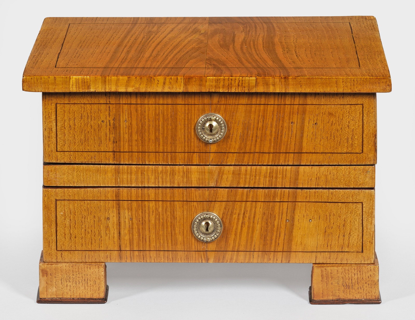 Biedermeier-Modellkommode: Eschenholz, furniert. Gerader, querrechteckig angelegter Korpus auf breiten, gekanteten Füßen. In der gegliederten Front zwei Schubladen. Rechteckige Deckplatte. H. 19 cm. 29 cm x 20 cm. A German as
