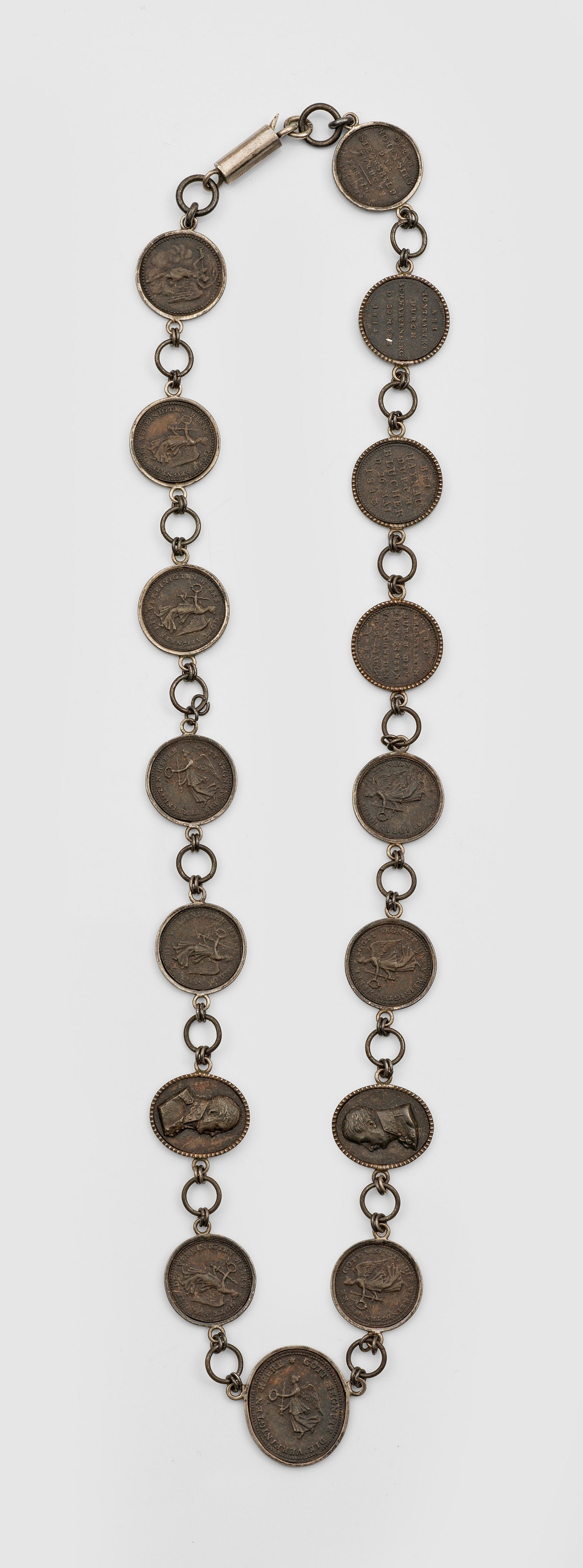Berliner Eisen-Collier mit Siegespfennigen: Eisen. 16 gefasste, durch runde Kettenglieder verbundene Medaillen, darunter 13 runde Siegespfennige aus den Jahren 1813 und 1814, ein ovaler Siegespfennig und zwei Porträtmedaillen mit Profildarstel