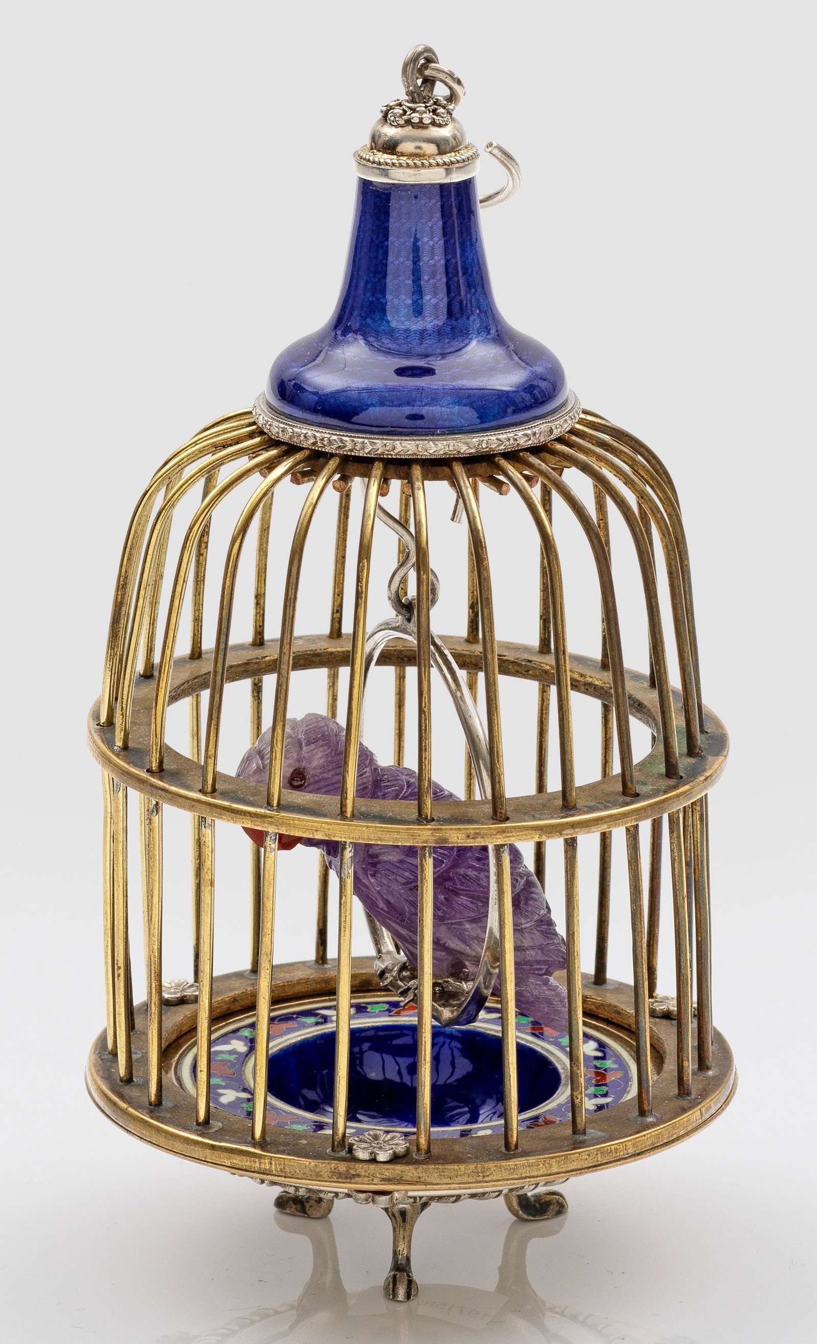 Kleiner Zierkäfig mit Papagei: im Stil von Karl Fabergé. Amethyst, Messing und Silber, teilw. emailliert. Über mittig vertieftem, auf blauem Grund polychrom emaillierter Silbersockel mit drei Tatzenfüßen, darauf zylindrischer K