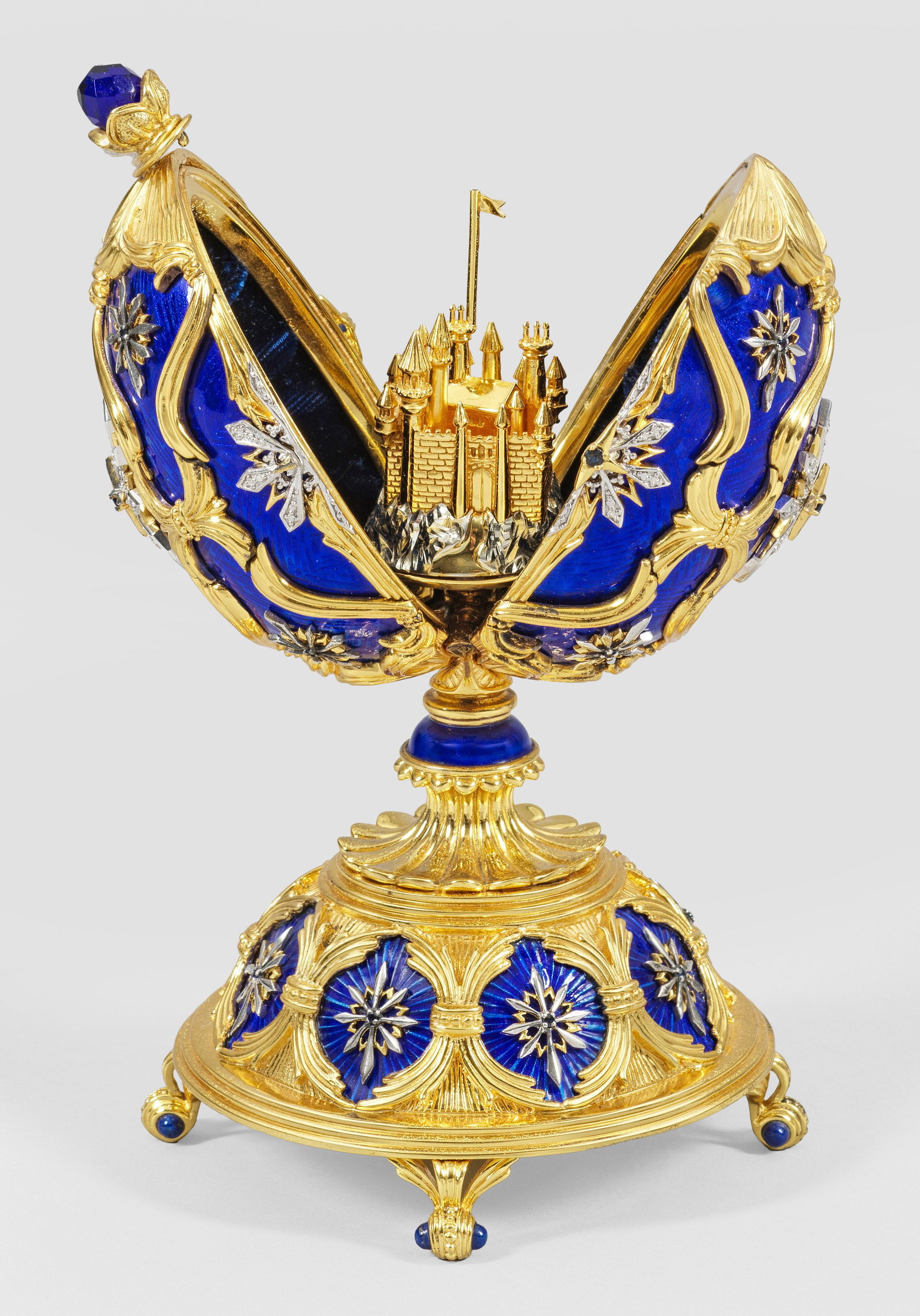 Spieluhr in Form eines Prunk-Eis: im Stil von Karl Fabergé. Sterlingsilber, vergoldet und teilw. dunkelblau emailliert. Über gewölbtem, von vier Volutenfüßen getragenem Stand und kurzem, in Palmetten ansetzendem Schaft ovoider, m