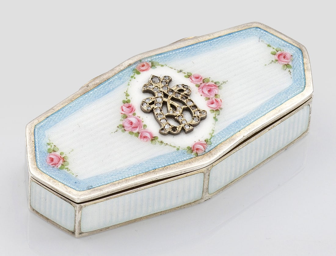 Emaildose mit Monogramm: im Stil von Karl Fabergé. Silber, teilw. vergoldet, teilw. emailliert. Achteckiger, querovaler Korpus, Wandung und Deckel überwiegend weiß emailliert mit hellblauem Zierrand und kleinen, polychrome