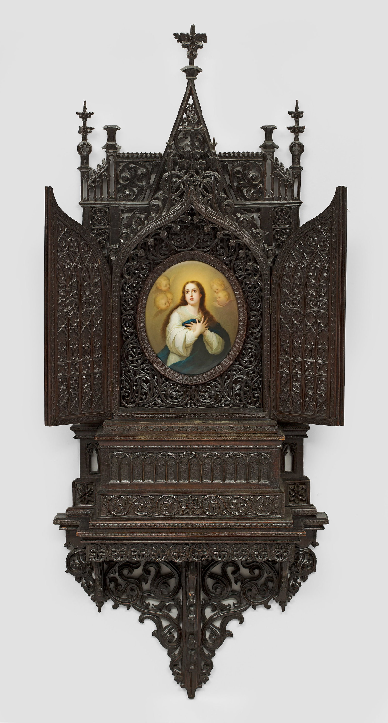 Neogotischer Hausaltar mit Porzellangemälde und Konsole: Holz, reich geschnitzt und ebonisiert. Zweitüriges Spitzbogenfeld über rechteckigem Sockel, gerahmt von architektonischen Elementen. Schauseitig flächendeckend, teilw. durchbrochen gearbeitet im ne