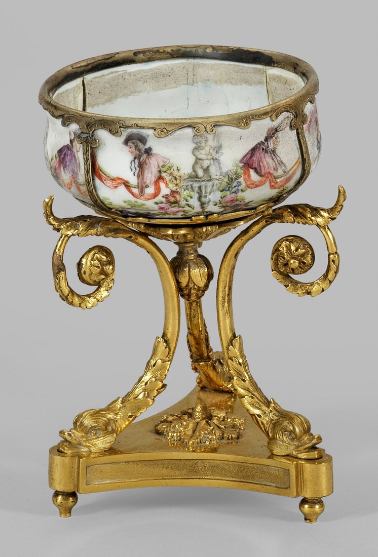 Kleine Aufsatzschale: Bronze, vergoldet. Von dreiseitigem Sockel aufsteigende, geschweifte Füße mit Delphinköpfen, oberhalb leicht gebauchte Porzellanschale mit unterschiedlichen Figurendarstellungen in polychromer Male