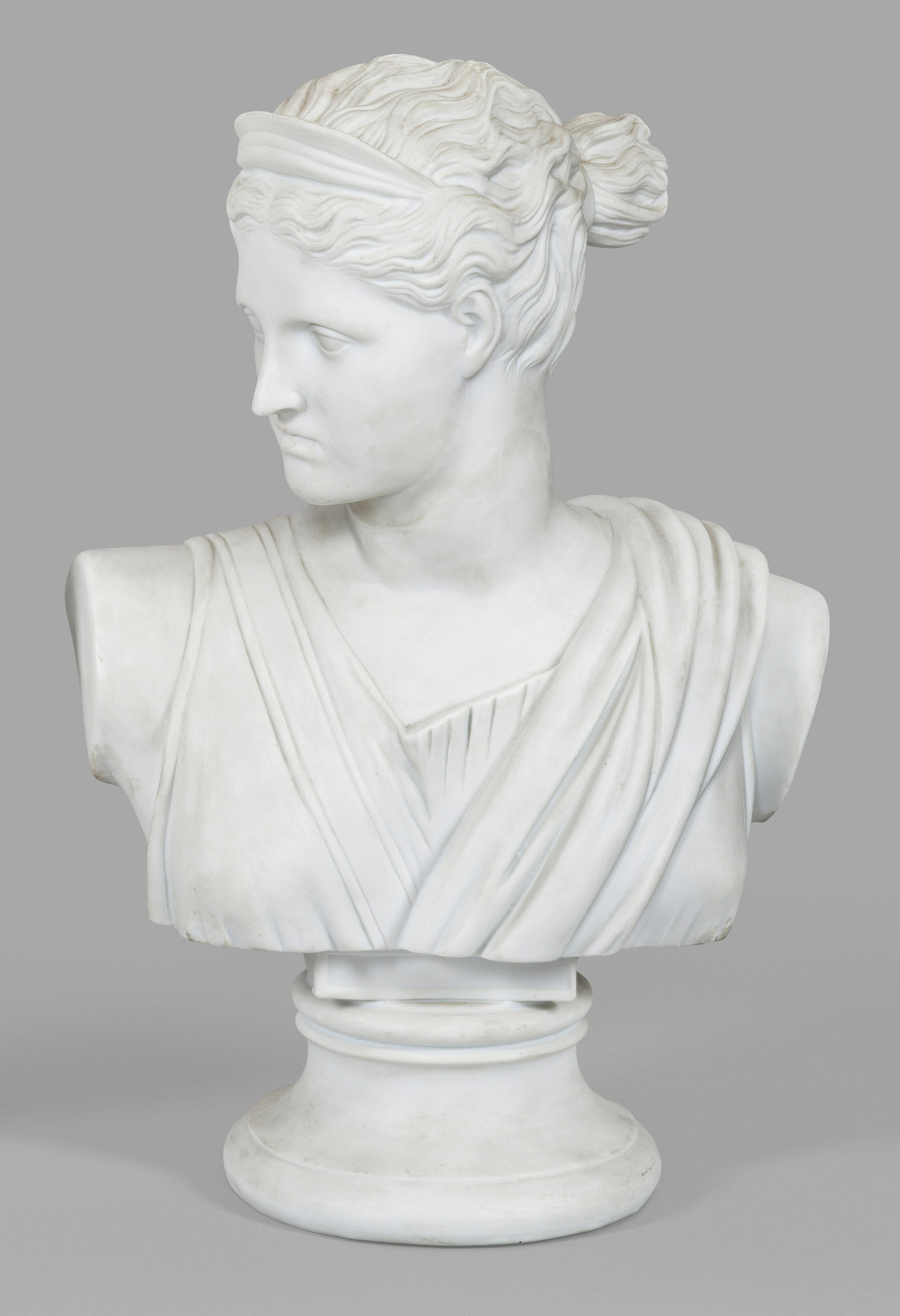 Diana-Büste: Biskuitporzellan. Über eingezogenem Rundsockel die Büste, der nach rechts gewandten Jagdgöttin, gestaltet in Anlehnung an die Diana von Versailles aus dem Louvre. Manufakturmarke. H. 43,5 cm. A bis