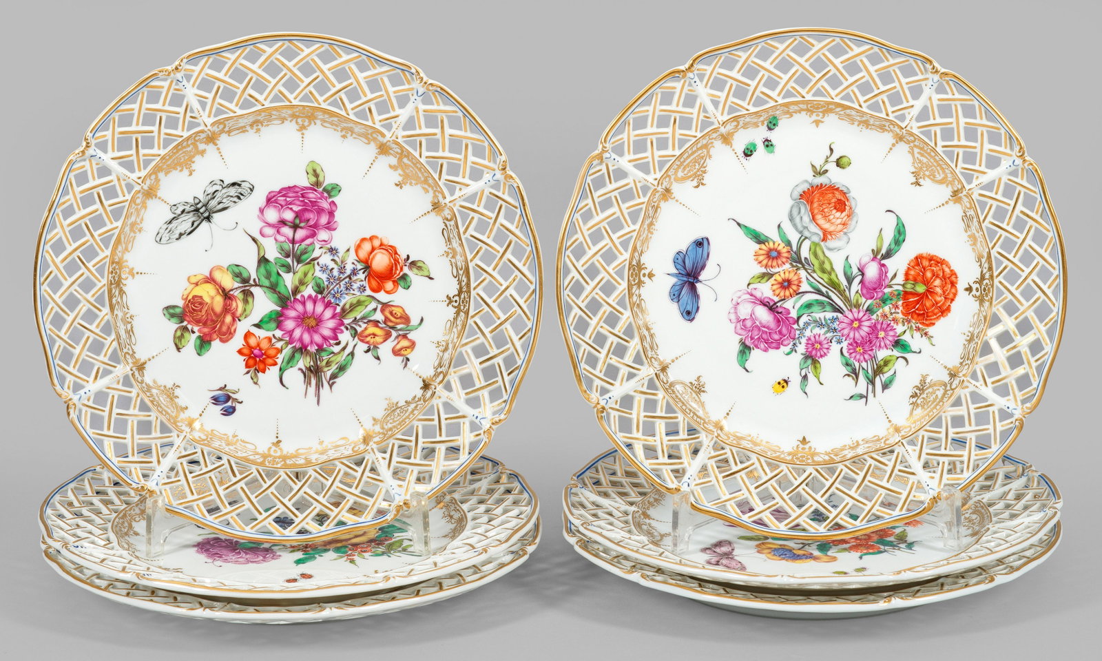 Sechs Zierteller mit Dekor "Cumberland": Runde, flach gemuldete Form mit faconniertem Rand. Korbgeflechtartig durchbrochen gearbeitete Fahne. Im Spiegel unterschiedliche, farbenfrohe Blumenbuketts, begleitet von großem Schmetterling. Leucht