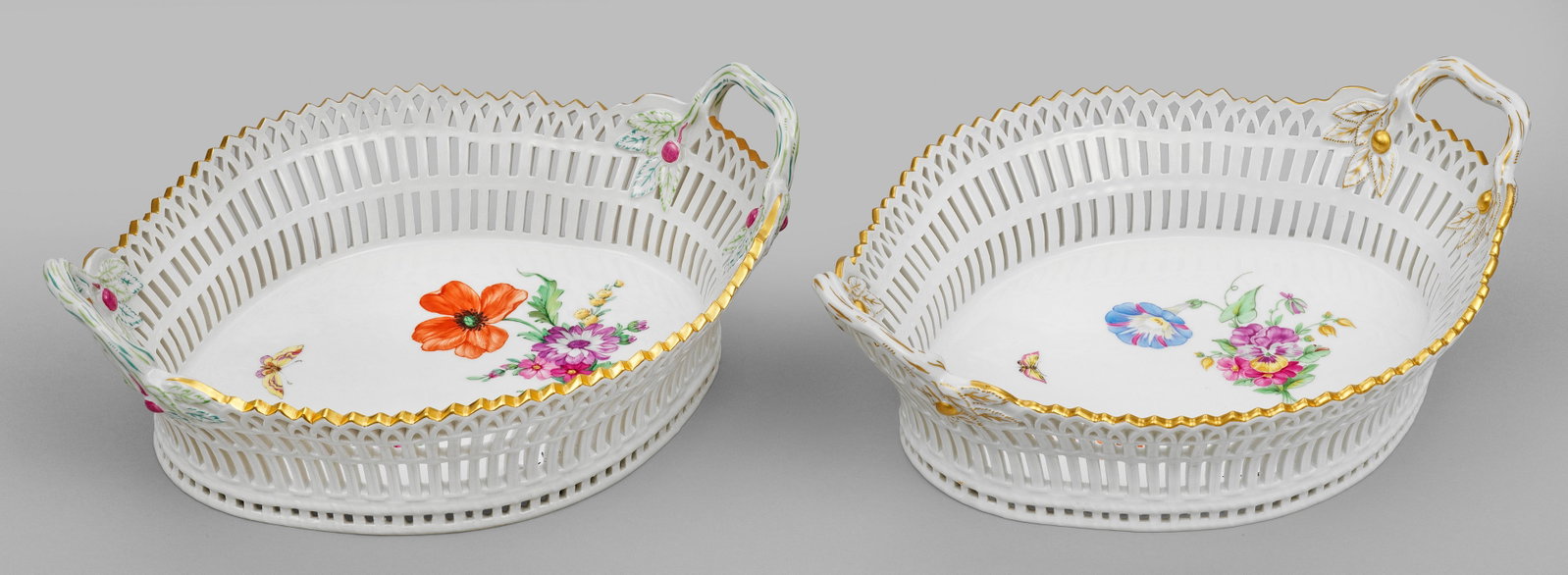 Paar Korbschalen mit Blumendekor: sog. "Englischer Fruchtkorb". Oval geschweifte Form mit durchbrochen gearbeiteter Wandung und astförmigen Henkeln. Im Spiegel Blumengebinde, Streublumen und ein Schmetterling in polychromer Malerei m