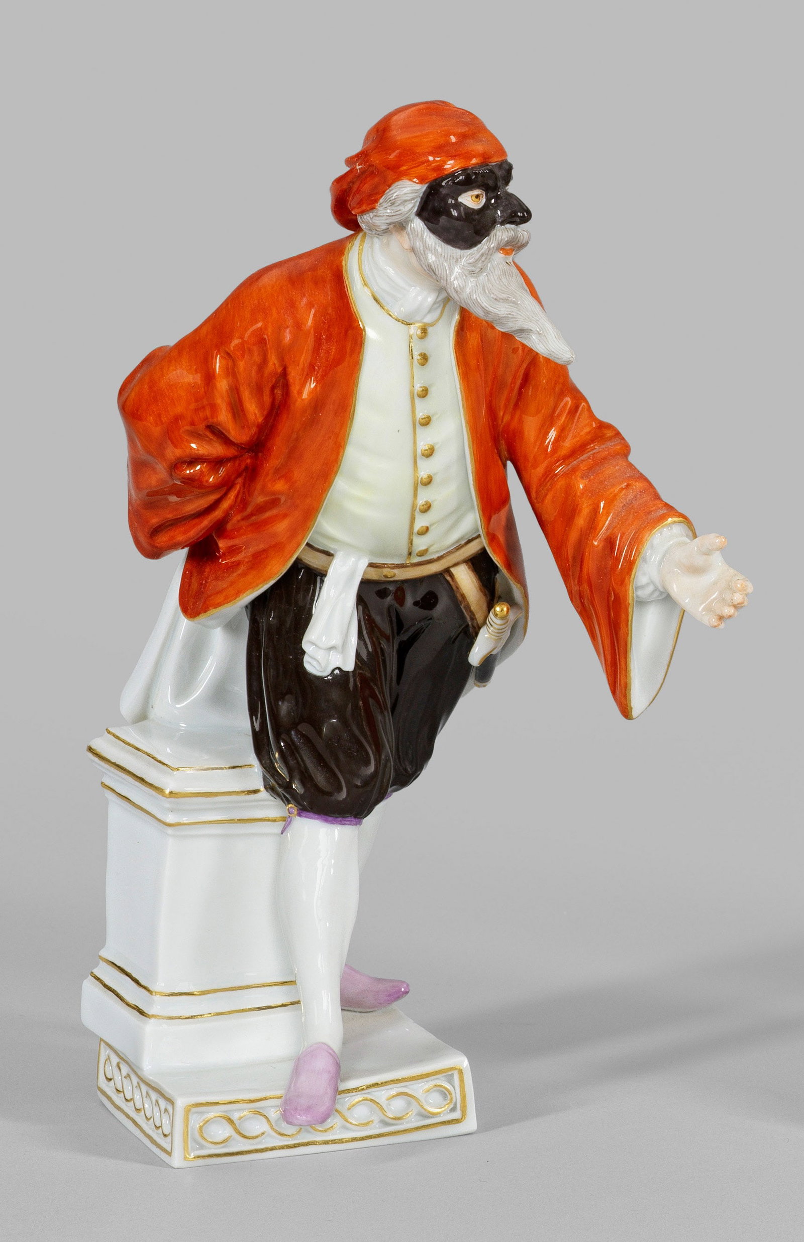 Pantalone aus der Italienischen Komödie: Auf quadratischer Plinthe stehender, spitzbärtiger Komödiant mit aufwendigem Kostüm, schwarzer Maske und Kappe. Polychrome Malerei mit Goldstaffage. Entw. Johann Joachim Kaendler. Modell-Nr. 64562.