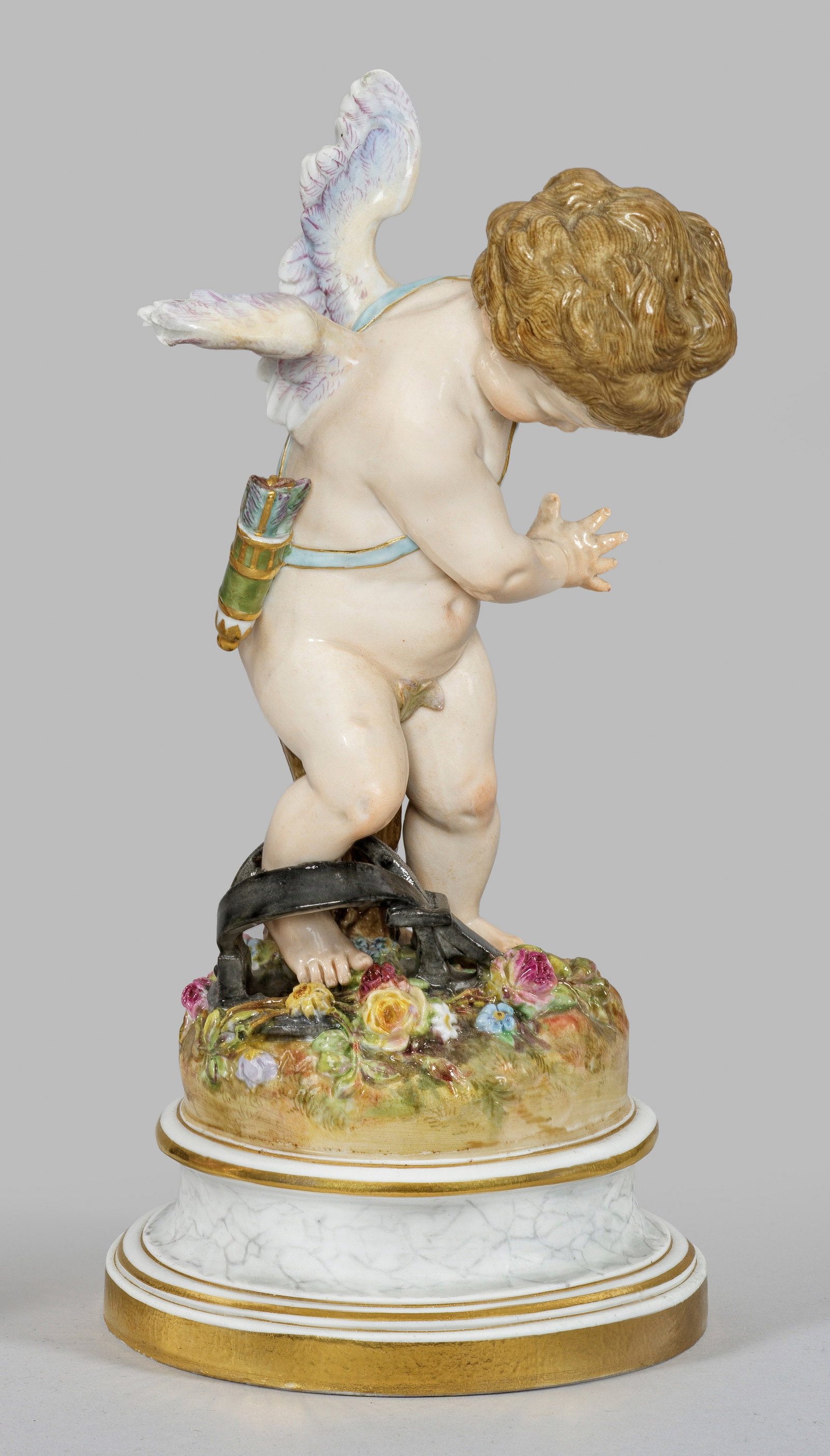 "Amor in der Falle". Originaltitel: Auf profiliertem, marmoriertem Rundsockel mit reliefplastischen Blüten stehender Amor, in eine Wildfalle tappend. Polychrome Malerei mit Goldstaffage. Entw. Heinrich Schwabe. Modell-Nr. L 120. Rest.;