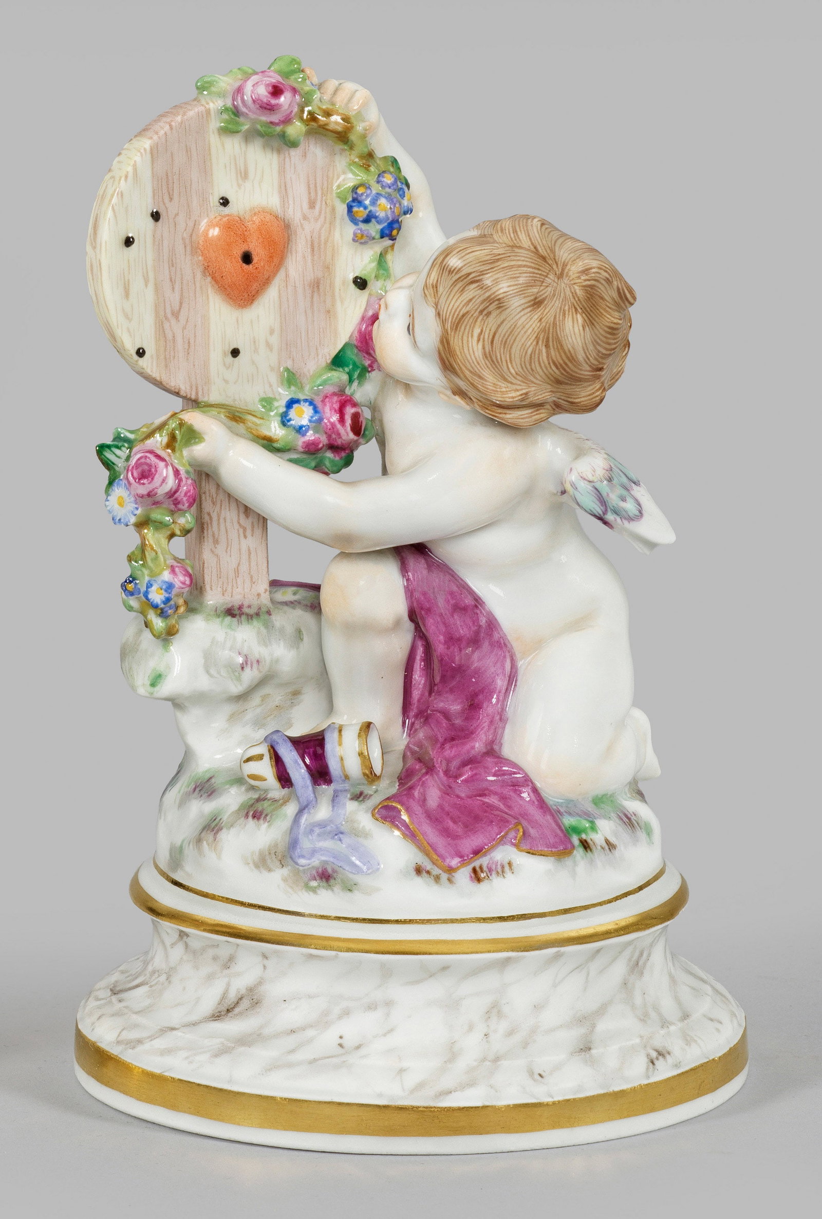 "Amor als Sieger". Originaltitel: Auf profiliertem, marmoriertem Rundsockel kniender, siegreicher Amor, eine Herz-Zielscheibe mit einer Blumengirlande schmückend. Polychrome Malerei mit Goldstaffage. Entw. Heinrich Schwabe. Modell-Nr
