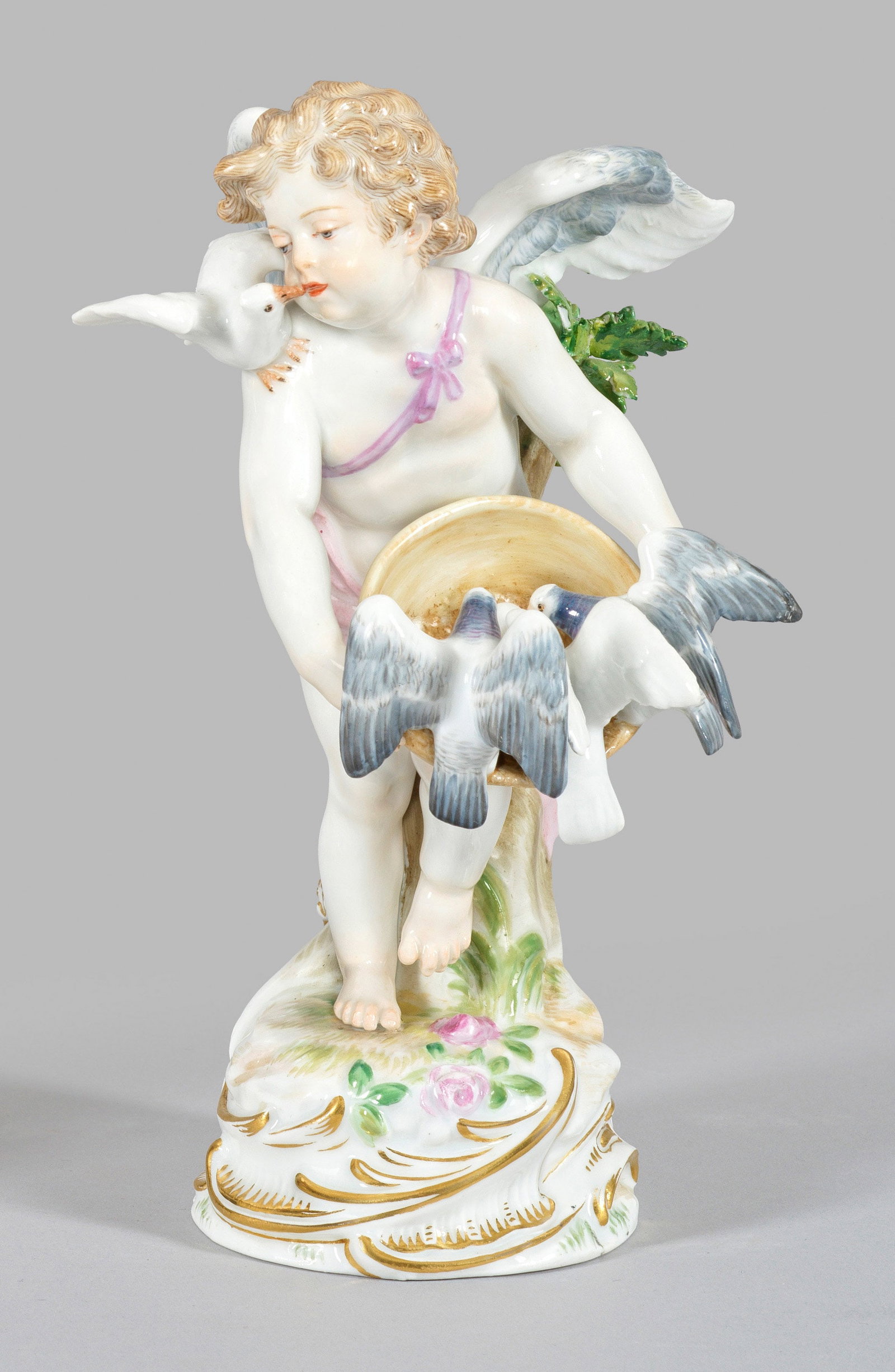 Amor mit Tauben: Auf gehöhtem, rocaillereliefiertem Sockel stehender, Tauben fütternder Amor. Polychrome Malerei mit Goldstaffage. Entw. Paul Helmig, 1898. Modell-Nr. R 122. Partiell best./rest.; Schwertermarke. H. 