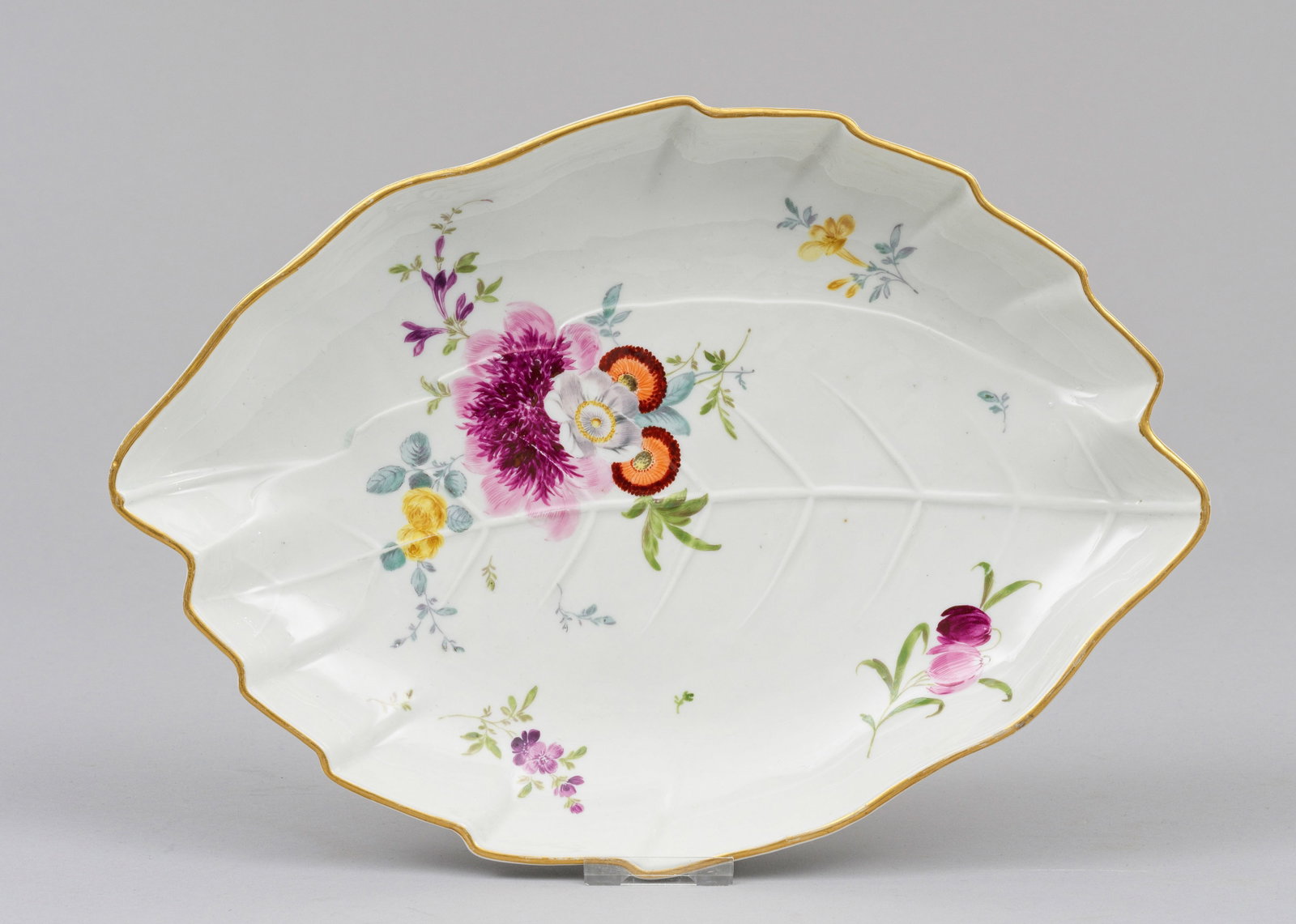 Blattschale mit Blumendekor: Ovale, leicht vertiefte Form mit passig geschweiftem Goldrand. Im Relief gearbeitete Blattadern. Im Spiegel Blumengebinde und Blüten in polychromer Malerei. Schwertermarke. 30,5 cm x 21 cm. A porcela