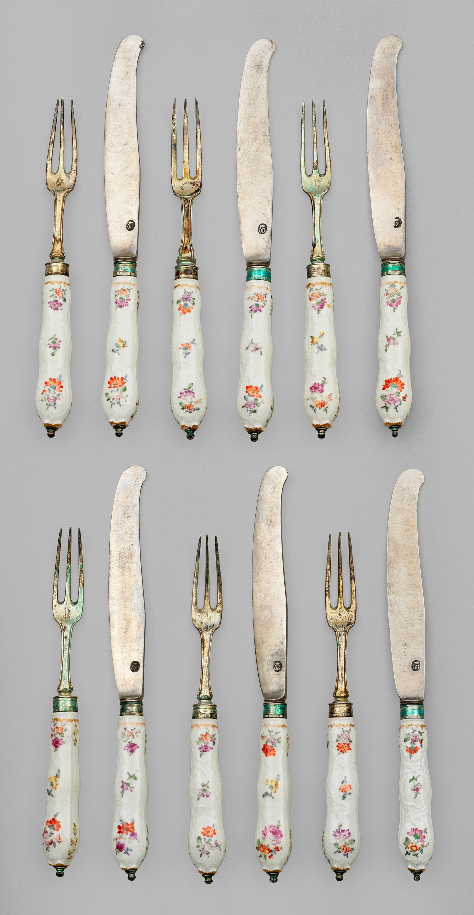 Tafelbesteck mit Blumendekor: 12-tlg.; 6 Gabeln und 6 Messer. Balusterförmige Porzellangriffe. Beidseitig der Wandung, zwischen reliefiertem Rocailledekor, farbenfrohe Blumengebinde und gestreute Blüten in polychromer Malerei mi