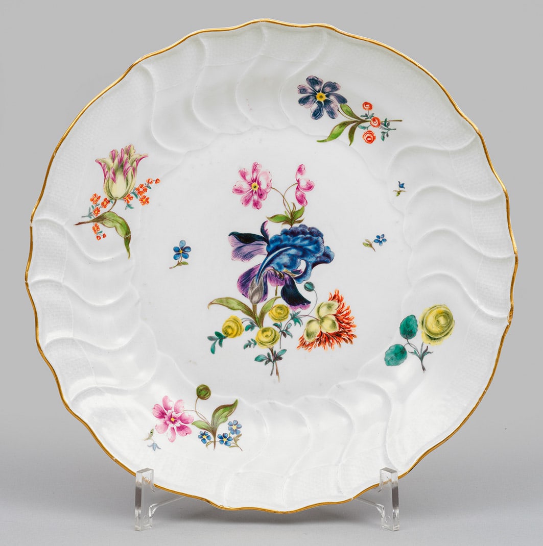 Teller mit Blumendekor: Runde, leicht vertiefte Form mit passig geschweiftem Goldrand. Reliefdekor "Neuozier". Im Spiegel und Steigbord Blumengebinde und Blüten und polychromer Malerei. Minim. best./rest.; Schwertermarke. D
