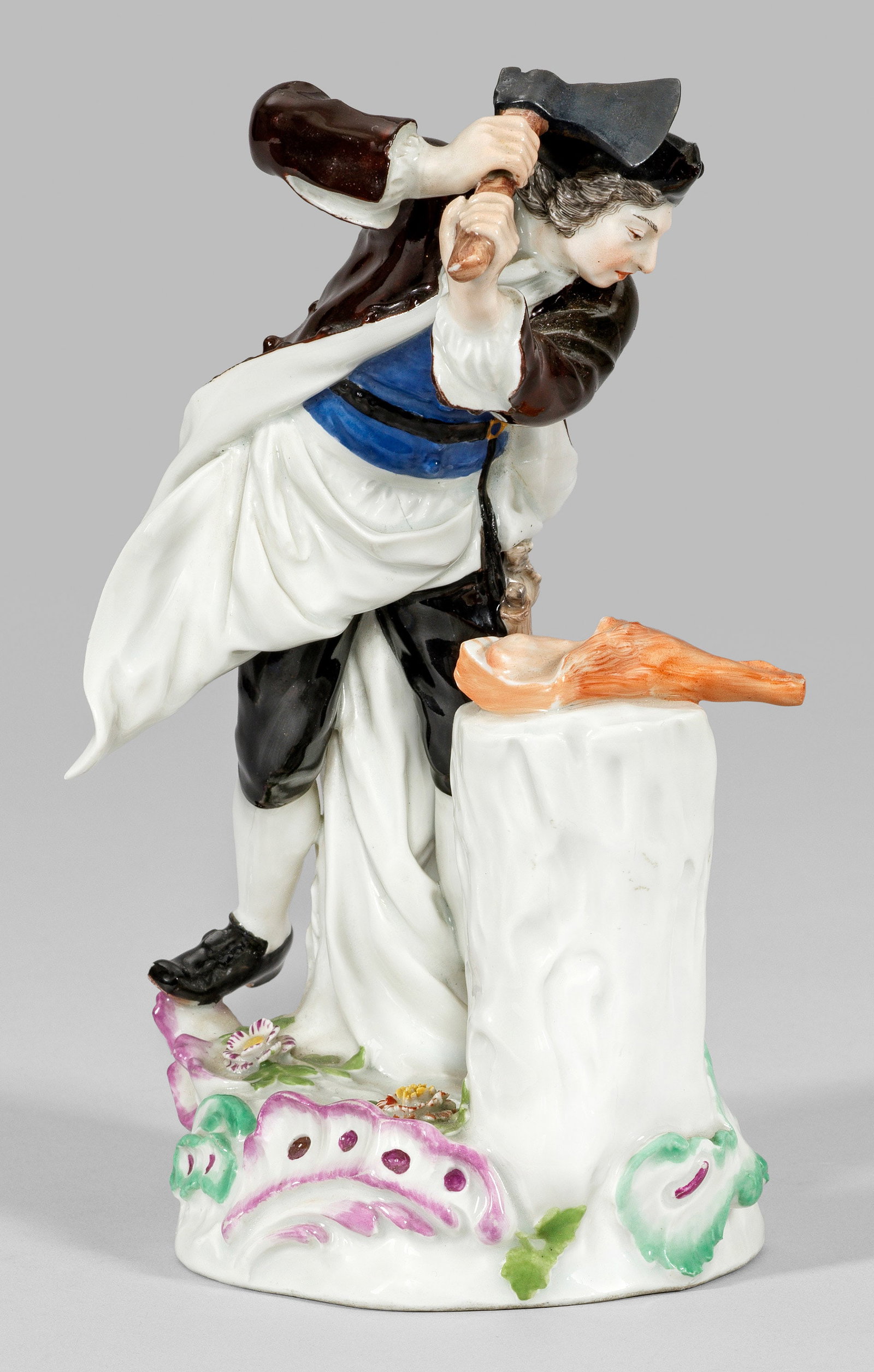 Fleischer-Figur: aus einer Serie von Handwerkern. Auf mit Blüten belegtem Rocaillesockel stehender Metzger mit Umhang und Schürze, im Begriff mit einem Beil die vor ihm auf einem Baumstumpf liegende Keule zu zerteil