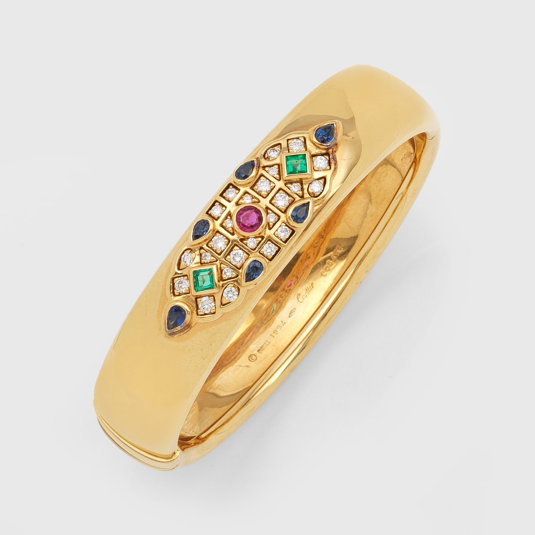 Multicolor Armreif von Cartier-"Saint Petersbourg" von 1994: Gelbgold, gest. 750. Leicht bombierter Armreif, schauseitig mosaikartig besetzt mit Saphiren, Rubinen und Smaragden von zus. ca. 1,50 ct., unterteilt durch Brillanten von zus. ca. 0,70 ct. (F-G/vvs). 