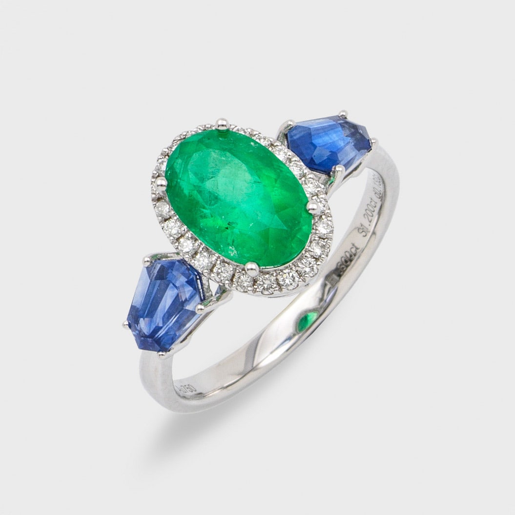 Feiner Saphir-Smaragd-Diamantring: Weißgold, gest. 750. Zentral besetzt mit einem leuchtendgrünen Smaragd von ca. 1,80 ct., entouriert von Diamanten von zus. ca. 0,13 ct., flankiert von 2 Saphir-Trapezen zus. ca. 1,20 ct.; Gew. ca. 3