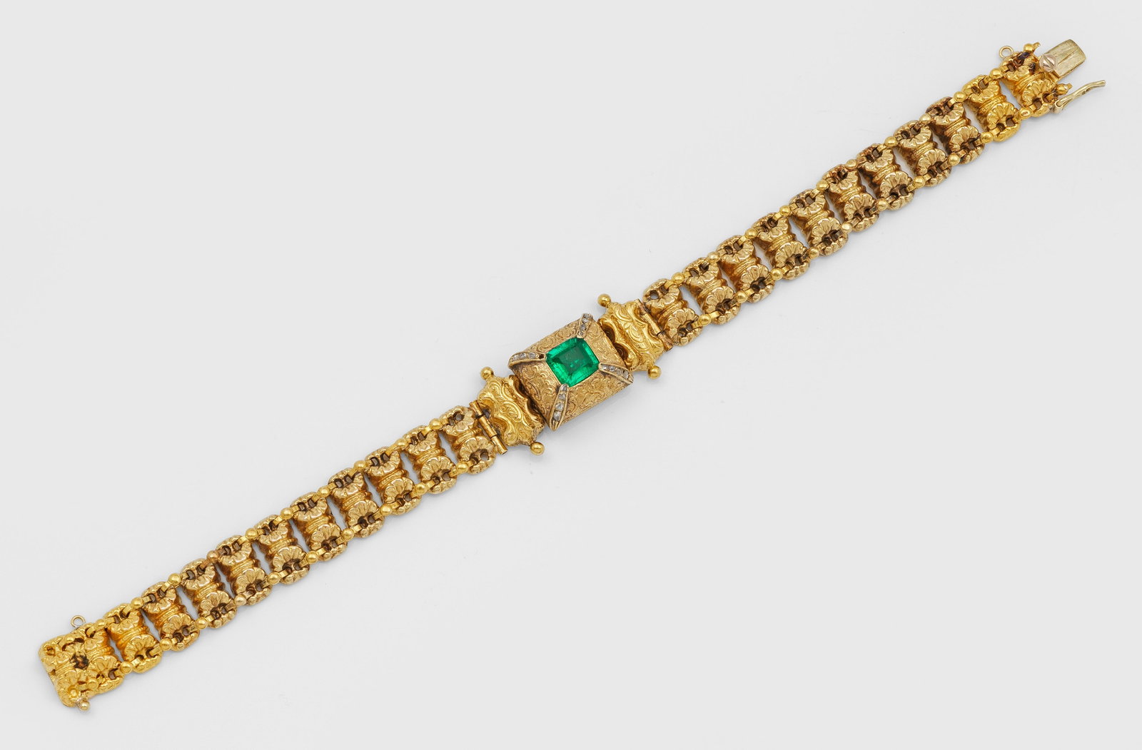 Belle Epoque Smaragd-Armband: Gelbgold, 18 ct.; Breite sog. Bandeau aus muschelförmig gefertigten Gliedern über kissenartigem, fein punzierten Mittelstück, besetzt mit einem leuchtendgrünen Smaragd von ca. 1,00 ct.,